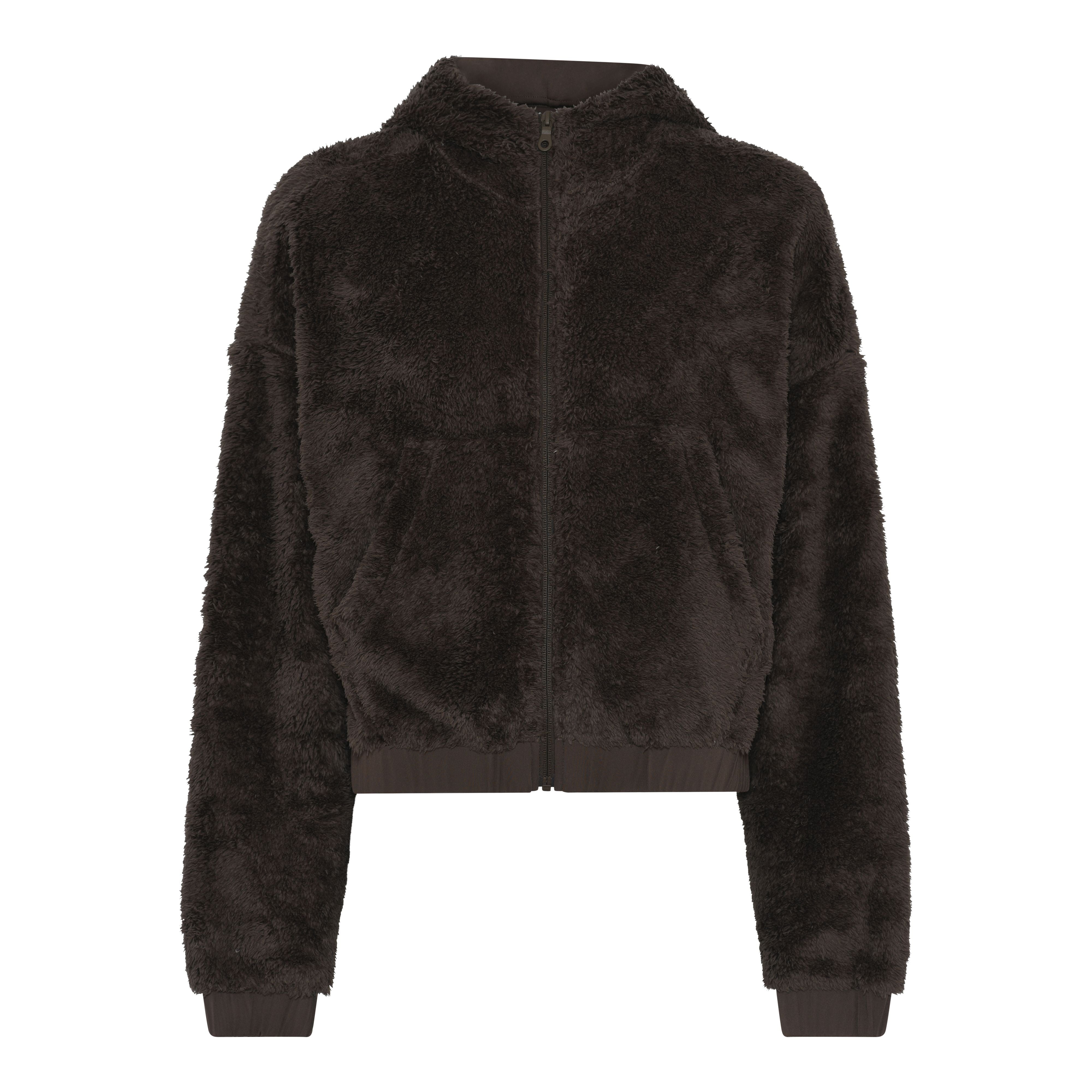 Dunkelbraune Fuzzy-Jacke mit Reißverschluss, hohem Kragen, langen Ärmeln, gerippten Ärmelbündchen und Saum, auf weißem Hintergrund.