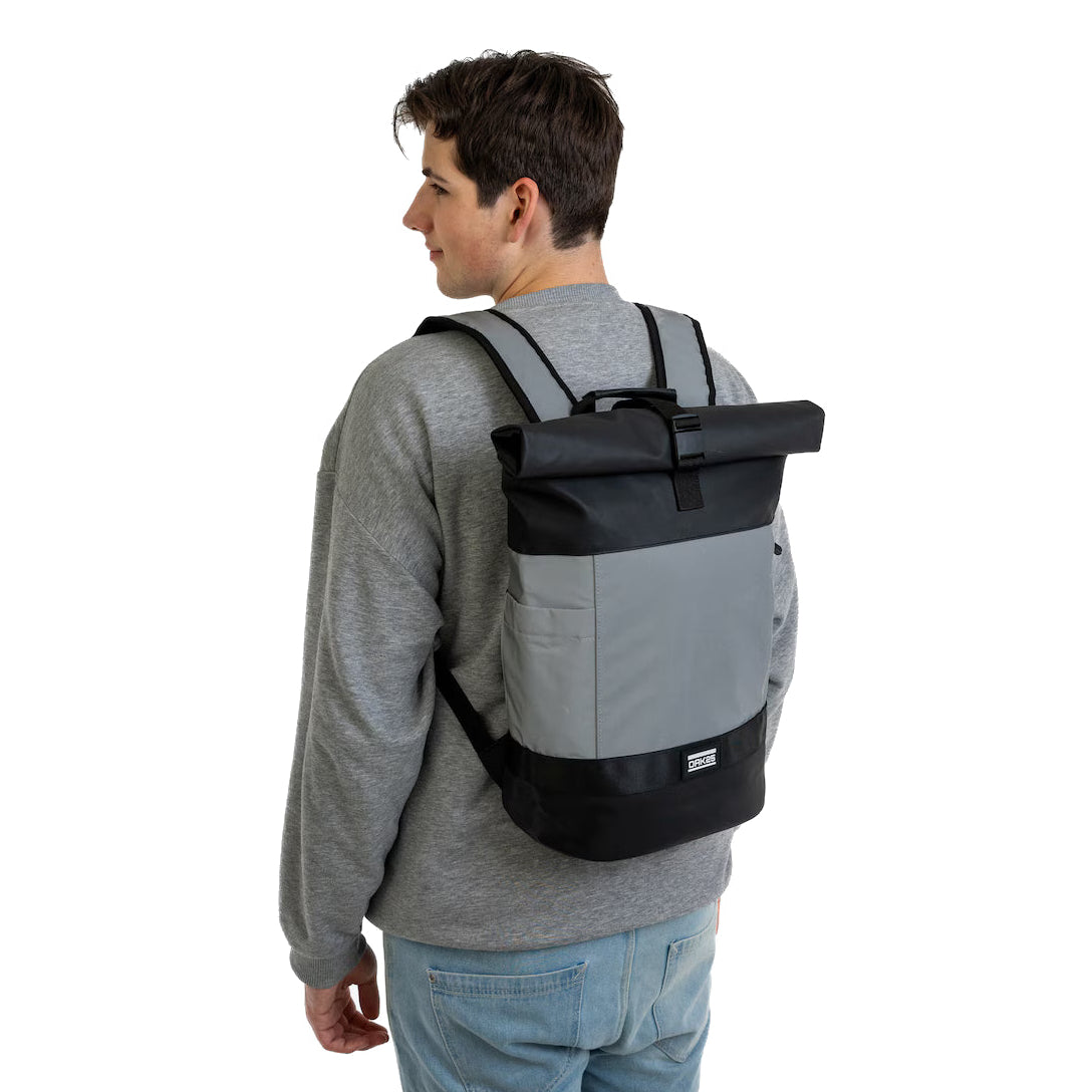 Eine Person, die ein graues Sweatshirt und eine blaue Jeans trägt, steht mit dem Gesicht nach hinten und trägt einen grau-schwarzen Rolltop-Rucksack auf dem Rücken vor einem weißen Hintergrund.