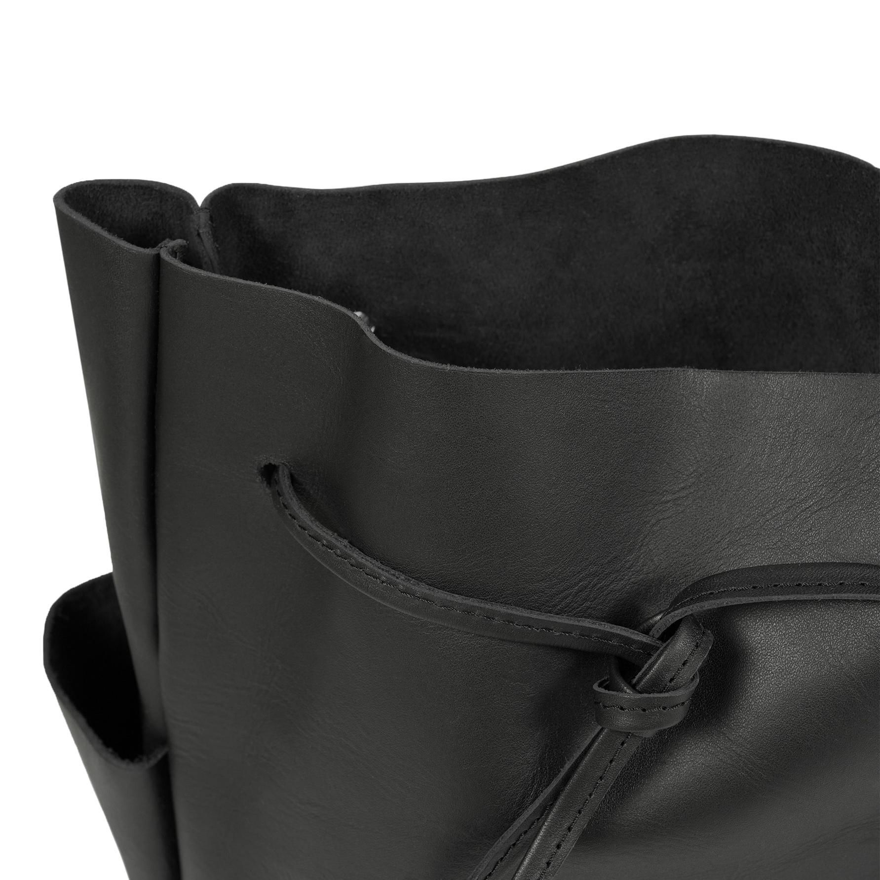 Nahaufnahme des oberen Teils einer schwarzen Ledertasche mit einem Kordelzugverschluss. Das Leder scheint glatt zu sein, und das Innere ist sichtbar und zeigt eine weiche, wildlederähnliche Textur.