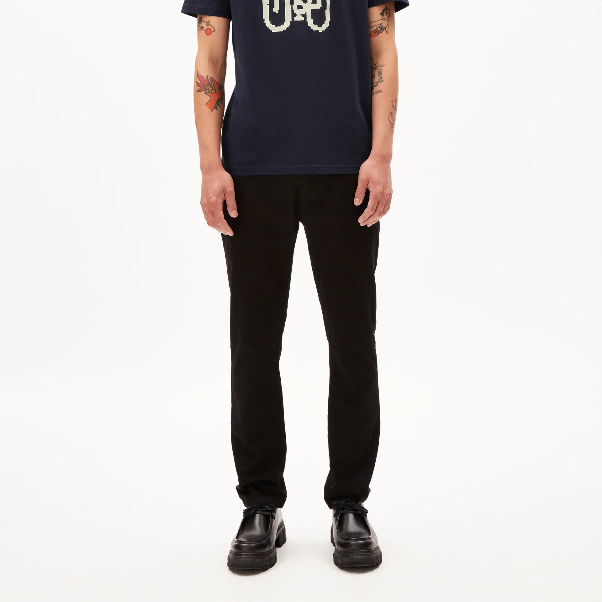 Eine Person mit kurzen Haaren, die ein marineblaues T-Shirt mit weißer Fahrradgrafik, eine schwarze Hose und schwarze Schuhe trägt, steht mit dem Gesicht nach vorne vor einem schlichten weißen Hintergrund.