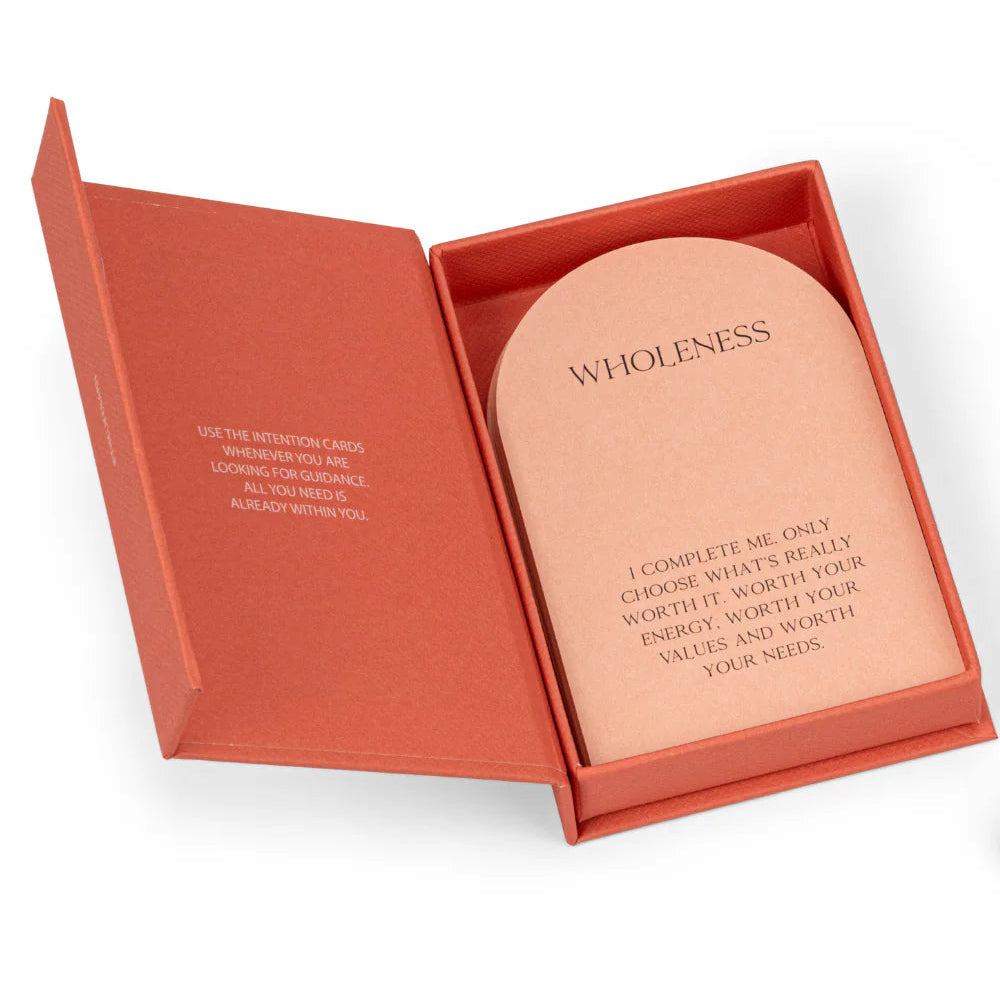 Eine korallenfarbene Schachtel mit einem aufgeklappten Deckel, der eine Karte mit der Aufschrift WHOLENESS (Ganzheitlichkeit) und einen Text über die Wahl dessen, was Ihrer Zeit, Energie und Werte wert ist, offenbart. Die Innenseite des Deckels enthält einen zusätzlichen motivierenden Text.