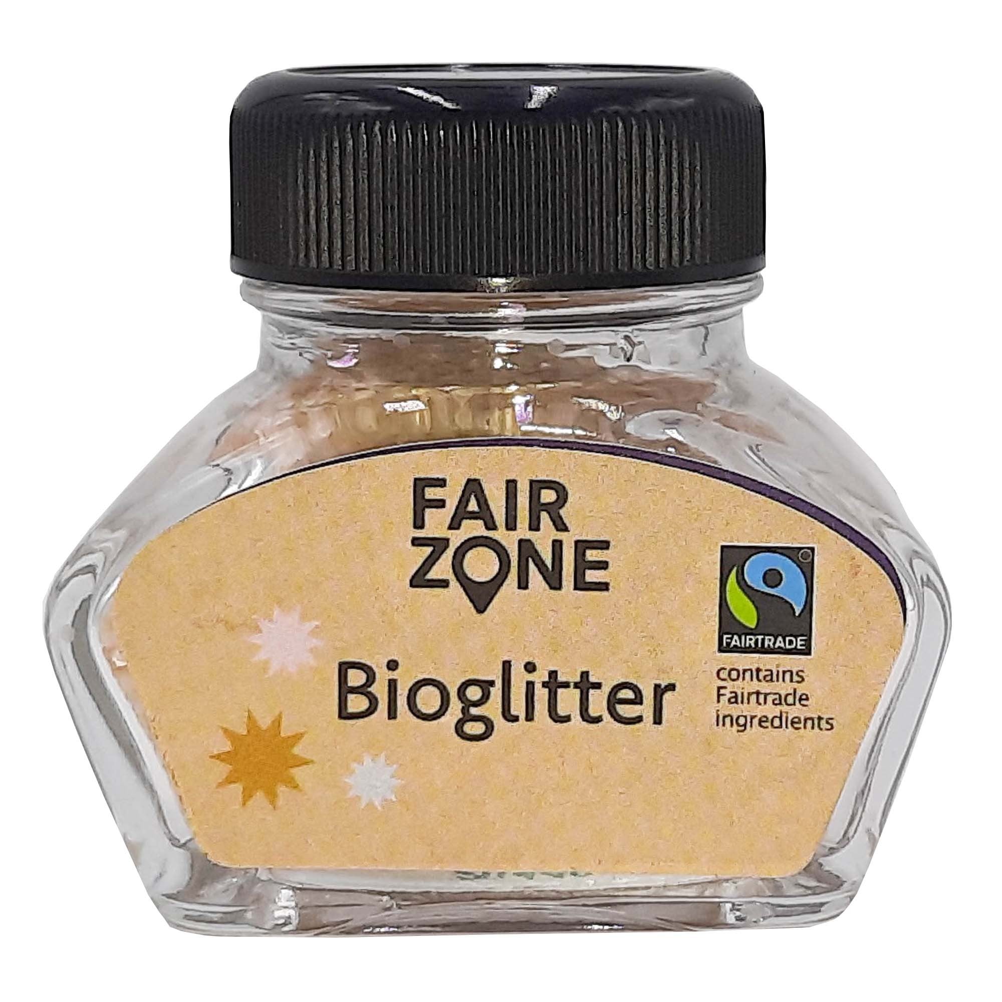Ein kleines durchsichtiges Glas mit der Aufschrift FAIR ZONE Bioglitter und einem schwarzen Deckel. Das Etikett enthält das Fairtrade-Logo und den Text, dass es Fairtrade-Zutaten enthält, mit dekorativen Sternen auf dem Etikett.