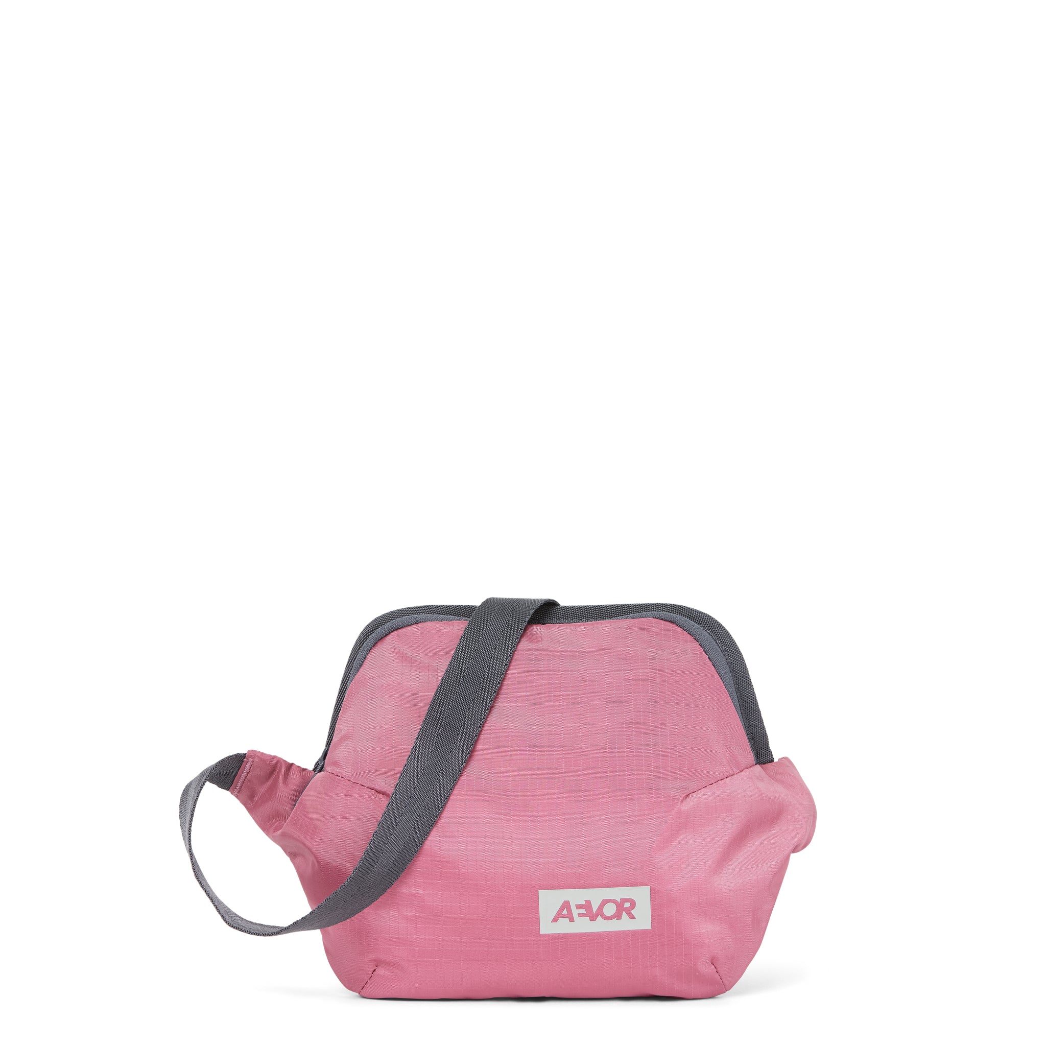 Eine kleine, hellrosa Umhängetasche mit einem grauen, verstellbaren Riemen und einem weißen Etikett mit der Aufschrift AEVOR auf der Vorderseite. Die Tasche hat ein einfaches, lässiges Design und ist vor einem schlichten weißen Hintergrund platziert.