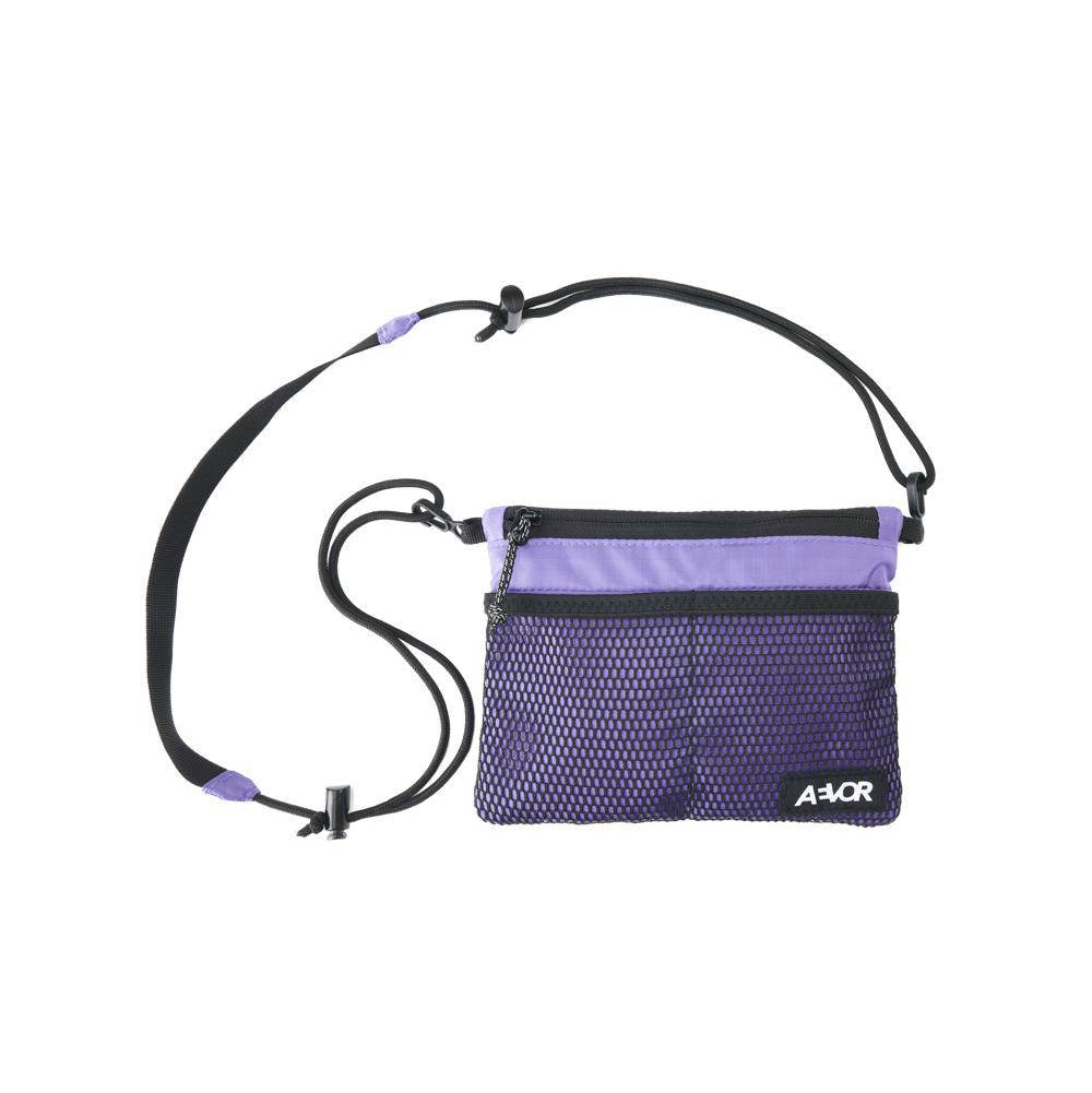Eine kleine, rechteckige, violette Umhängetasche mit einem verstellbaren schwarzen Riemen, einer Netztasche auf der Vorderseite, Reißverschlüssen und einem weißen A4OR-Logo in der unteren rechten Ecke.