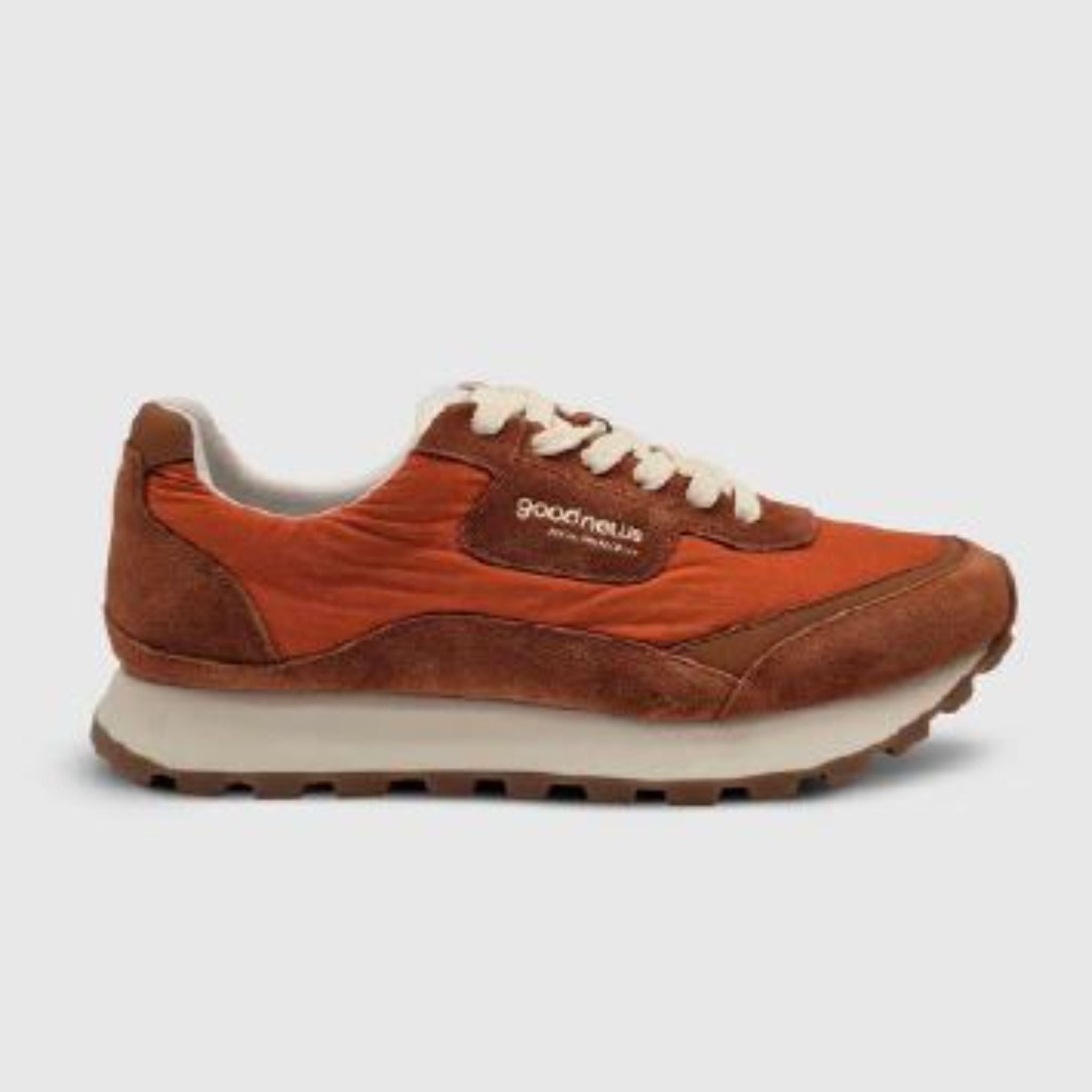 Ein einzelner orangefarbener und brauner Sneaker mit weißen Schnürsenkeln, weißer Zwischensohle und einer braunen, strukturierten Sohle. An der Seite des Schuhs befindet sich das Good-News-Logo. Der Hintergrund ist hellgrau.