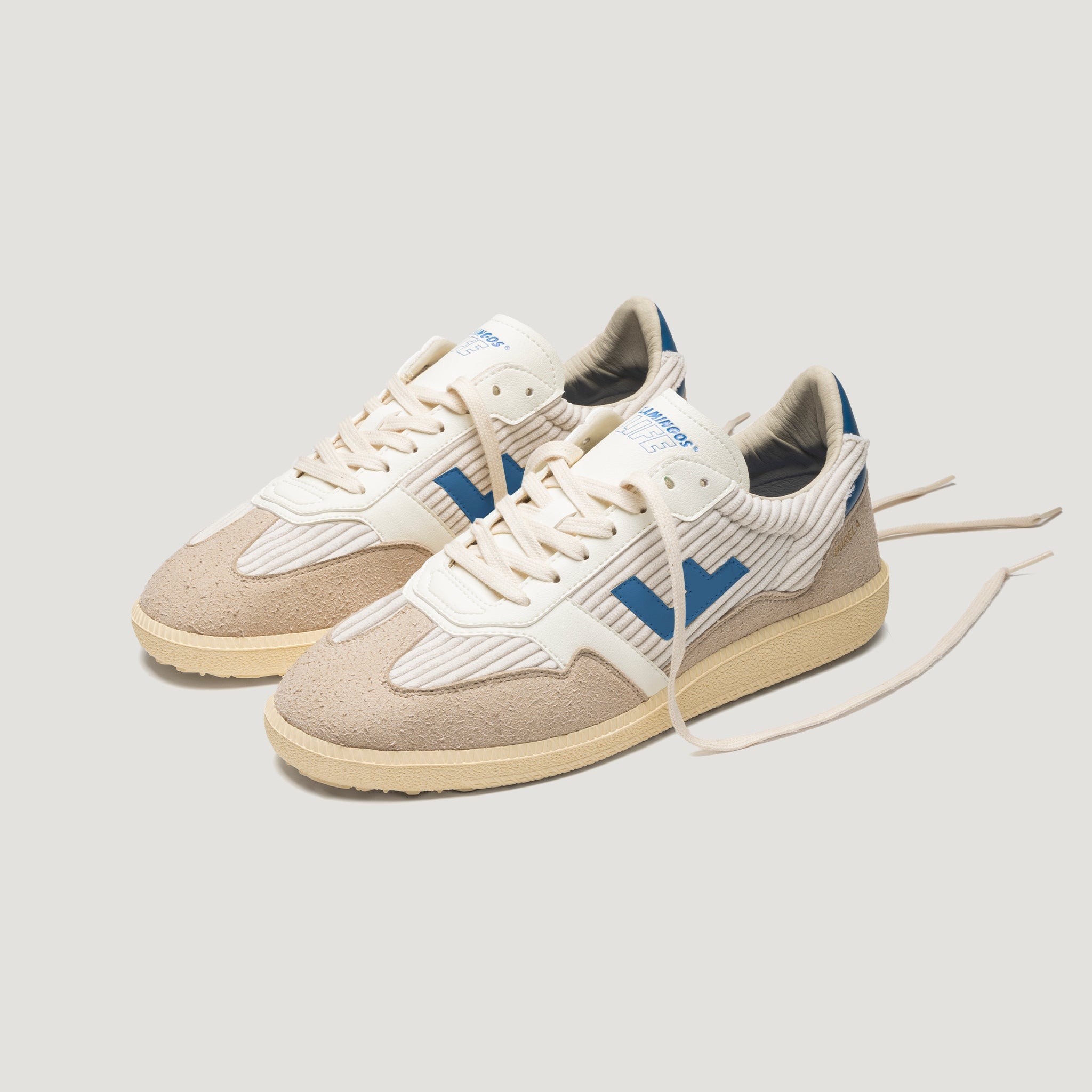 Ein Paar beige-weiße Turnschuhe mit blauen Akzenten und hellbraunen Sohlen, mit strukturiertem Wildleder an den Zehen und an den Seiten und weißen Schnürsenkeln auf hellgrauem Hintergrund.