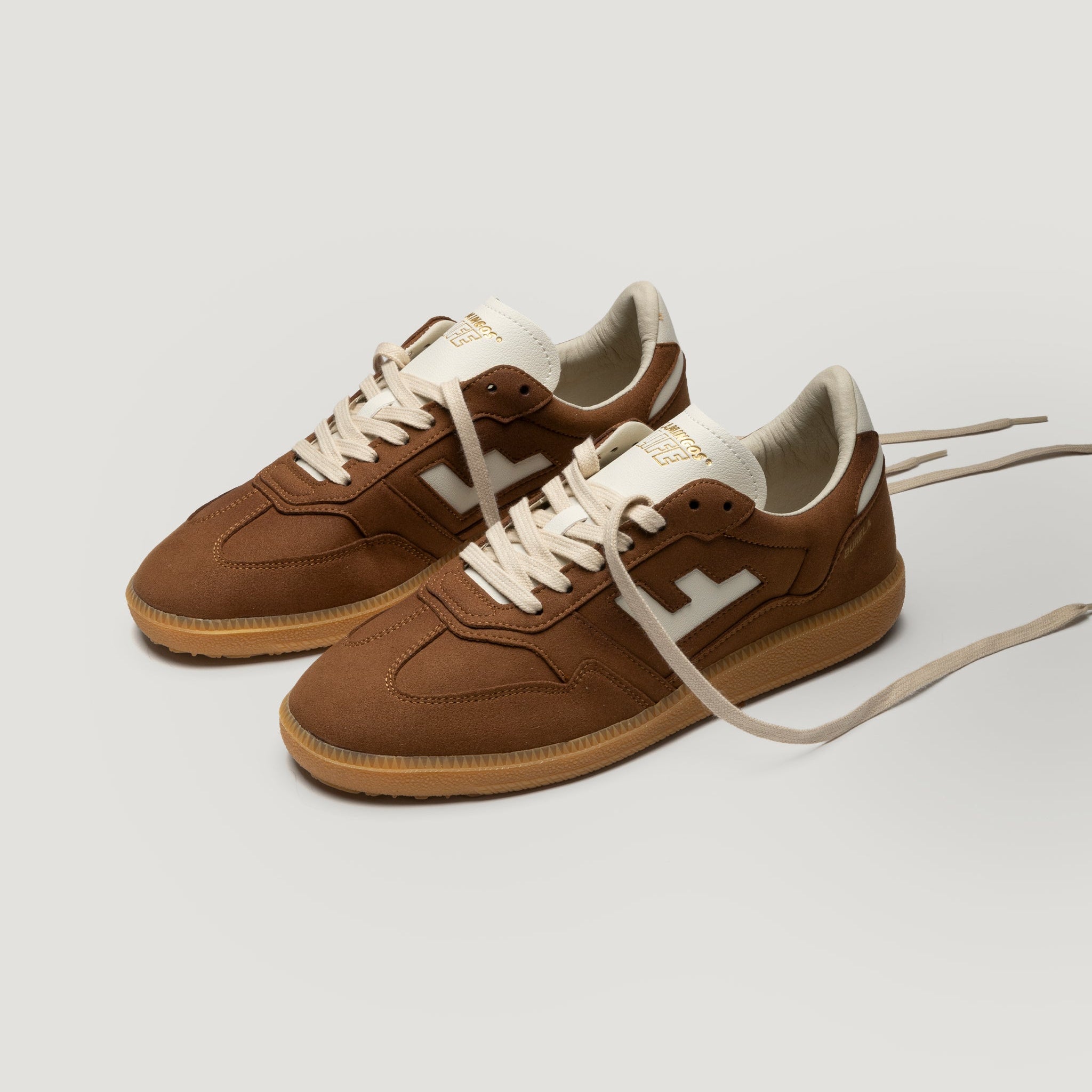 Ein Paar braune Low-Top-Sneaker mit beigen Schnürsenkeln, cremefarbener Zunge und Futter, weißem Zickzack-Logo an der Seite und Gummisohlen auf hellgrauem Hintergrund.