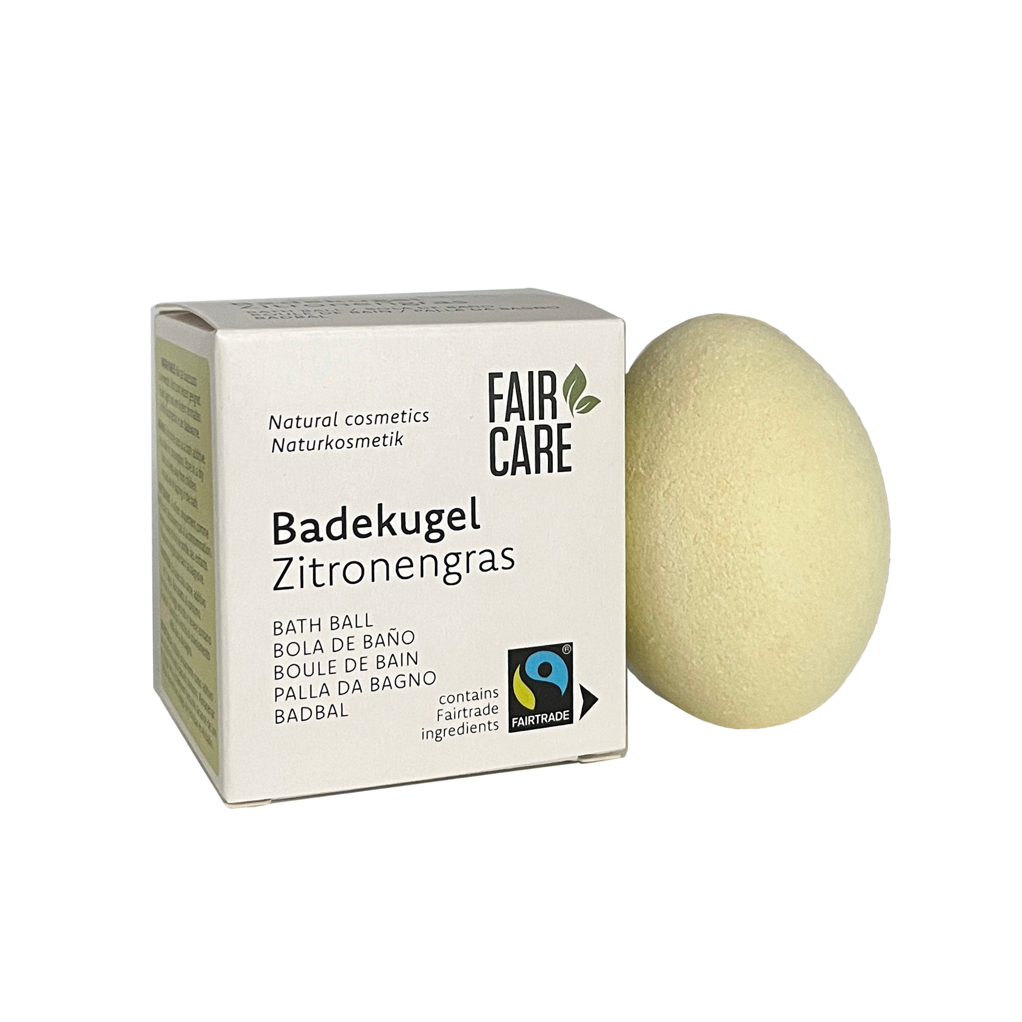 Eine blassgelbe Badekugel neben einer weißen Schachtel mit der Aufschrift FAIR CARE Badekugel Zitronengras, die darauf hinweist, dass es sich um eine Zitronengras-Badekugel mit Fairtrade-Zutaten und Naturkosmetik handelt.