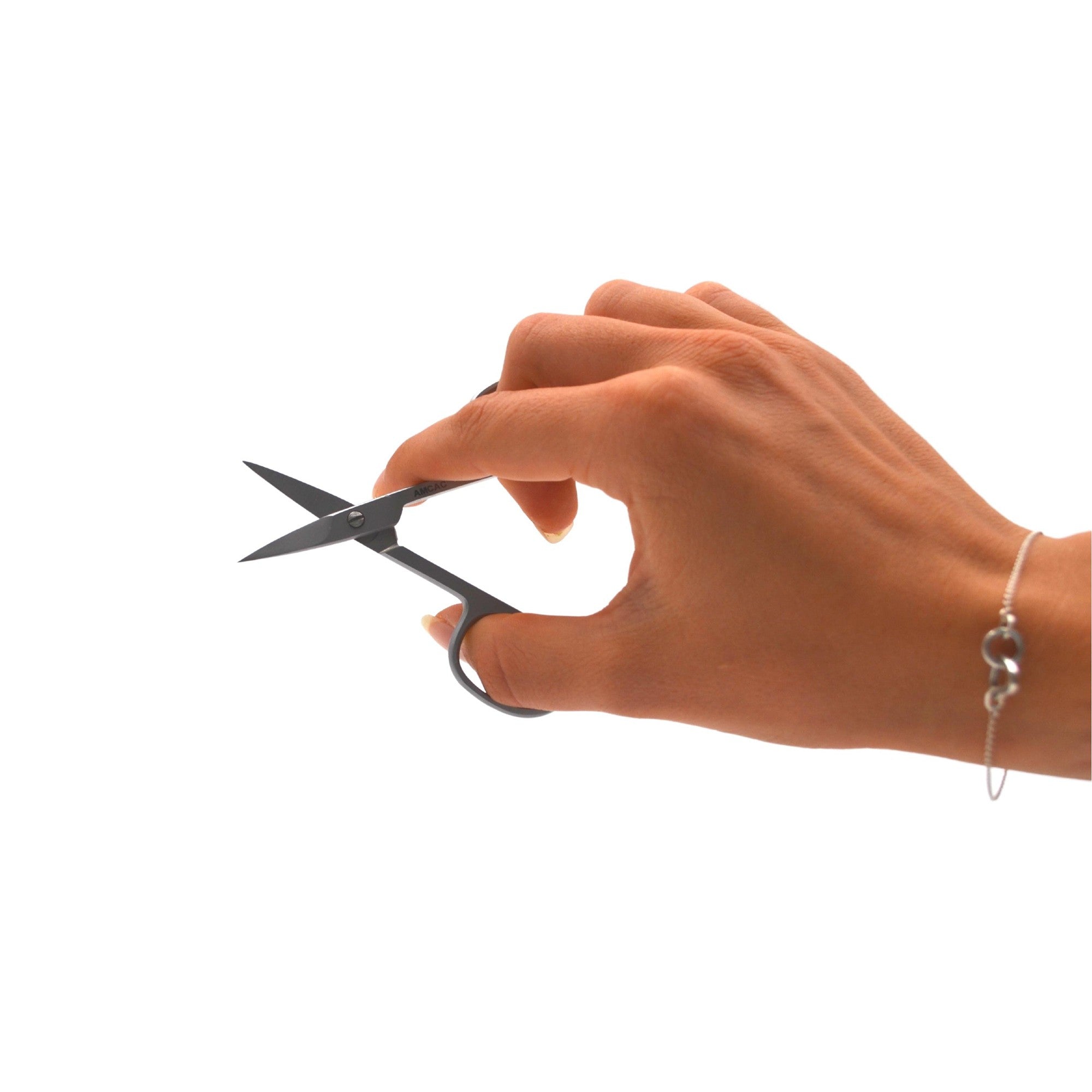 Eine Hand mit einem Armband, die eine kleine Schere hält, mit geöffneten Klingen vor einem schlichten weißen Hintergrund.