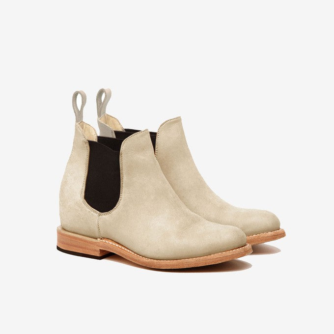 Ein Paar hellbeige Chelsea-Stiefel aus Wildleder mit elastischen schwarzen Seitenteilen, hellbraunen Ledersohlen und Zuglaschen auf der Rückseite, dargestellt auf einem schlichten weißen Hintergrund.