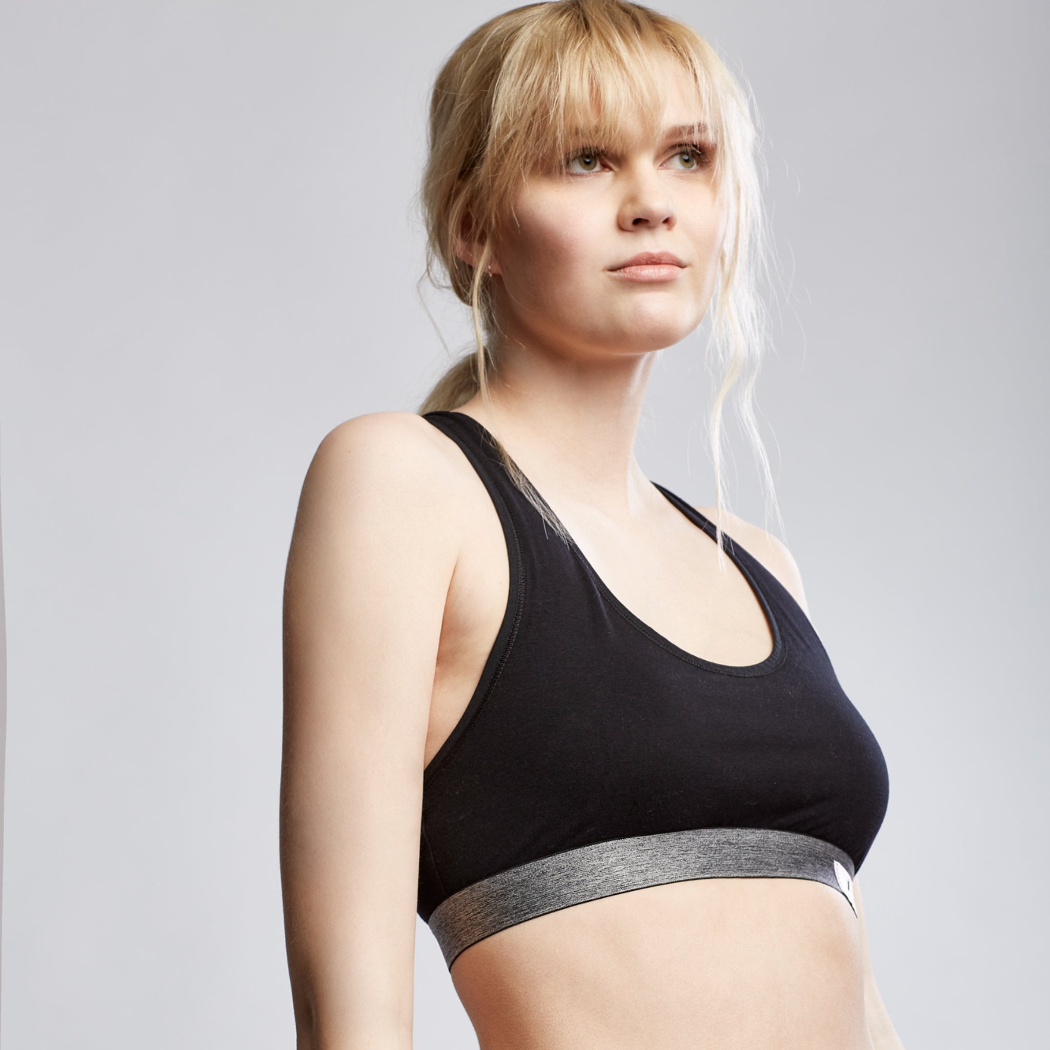 Eine Frau mit blonden Haaren trägt ein schwarzes Sporttop und blickt ernst seitwärts auf einem neutralen Hintergrund.