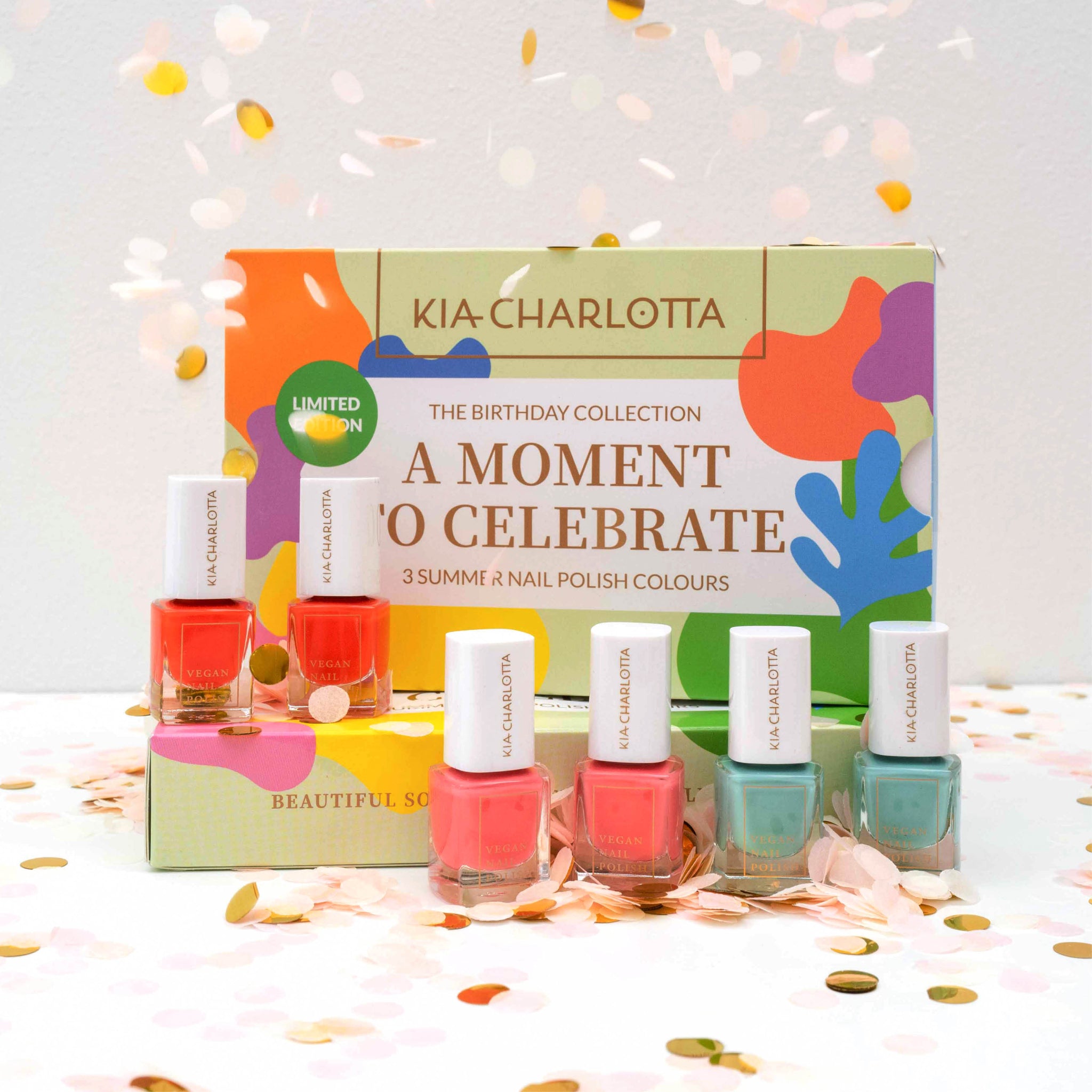 Bunte Nagellackflaschen stehen vor einer dekorativen Box von "Kia-Charlotta", umgeben von Konfetti.