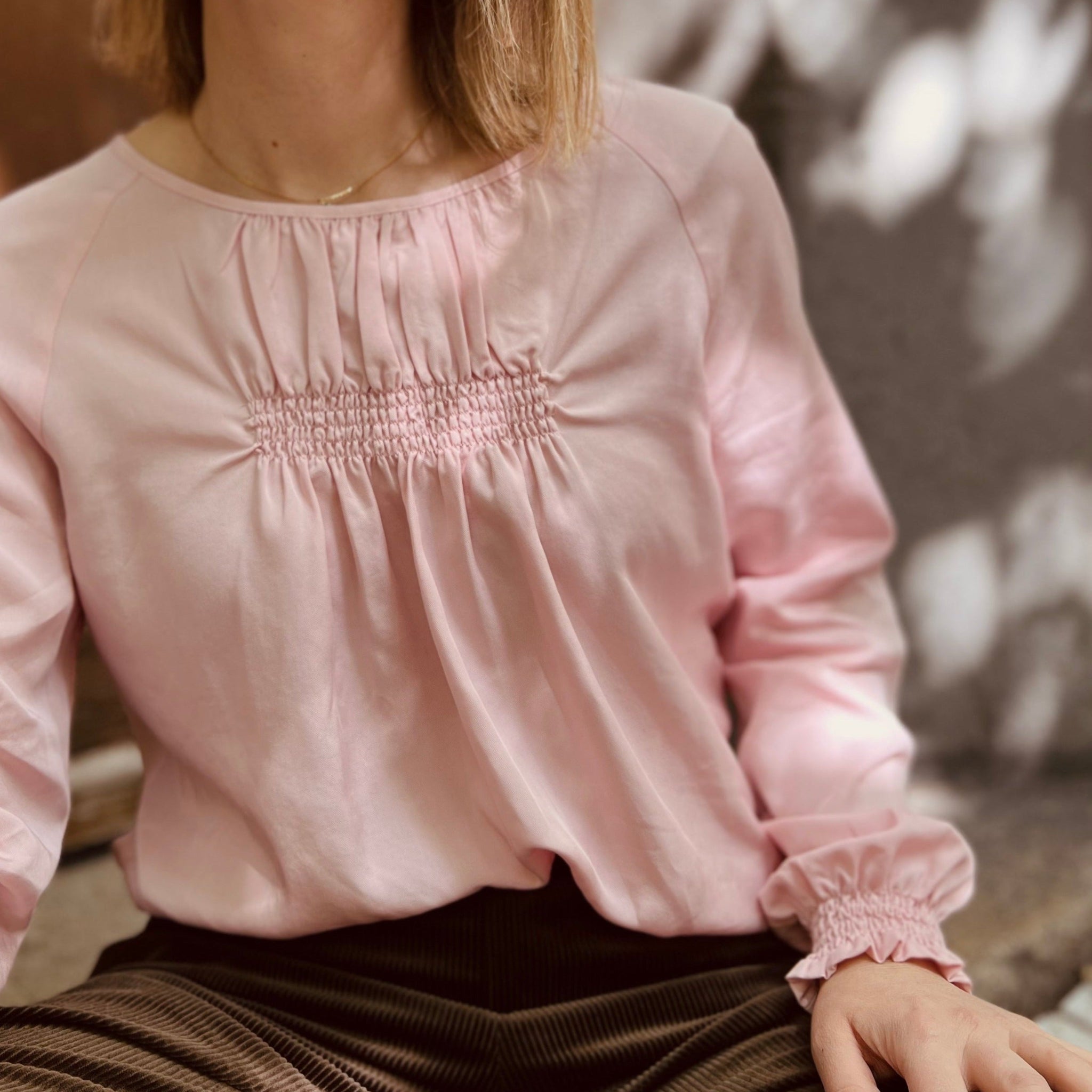 Person in rosa Bluse mit gerafftem Detail, sitzt in einem schattigen Bereich.