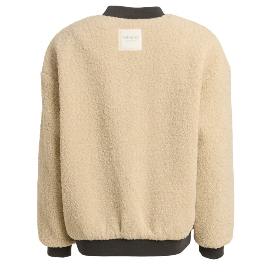 Eine beigefarbene Sherpa-Fleecejacke mit lockerer Passform, langen Ärmeln und schwarzen Rippbündchen an Ärmeln und Saum. Auf der Rückseite befindet sich ein kleiner weißer rechteckiger Aufnäher in der Nähe des Halsausschnitts.