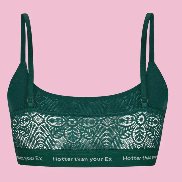 Ein dunkelgrüner Spitzen-Bralette mit verschlungenen Mustern und dünnen Trägern, die sich vor einem rosa Hintergrund abzeichnen. Auf dem unteren Band steht in weißen Lettern "Hotter than your Ex".