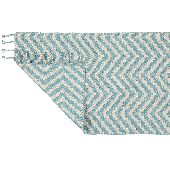 Ein rechteckiger Teppich mit blauem und weißem Zickzackmuster, der an einer Ecke teilweise gefaltet ist. Der Teppich hat kleine Quasten entlang der kürzeren Kante.