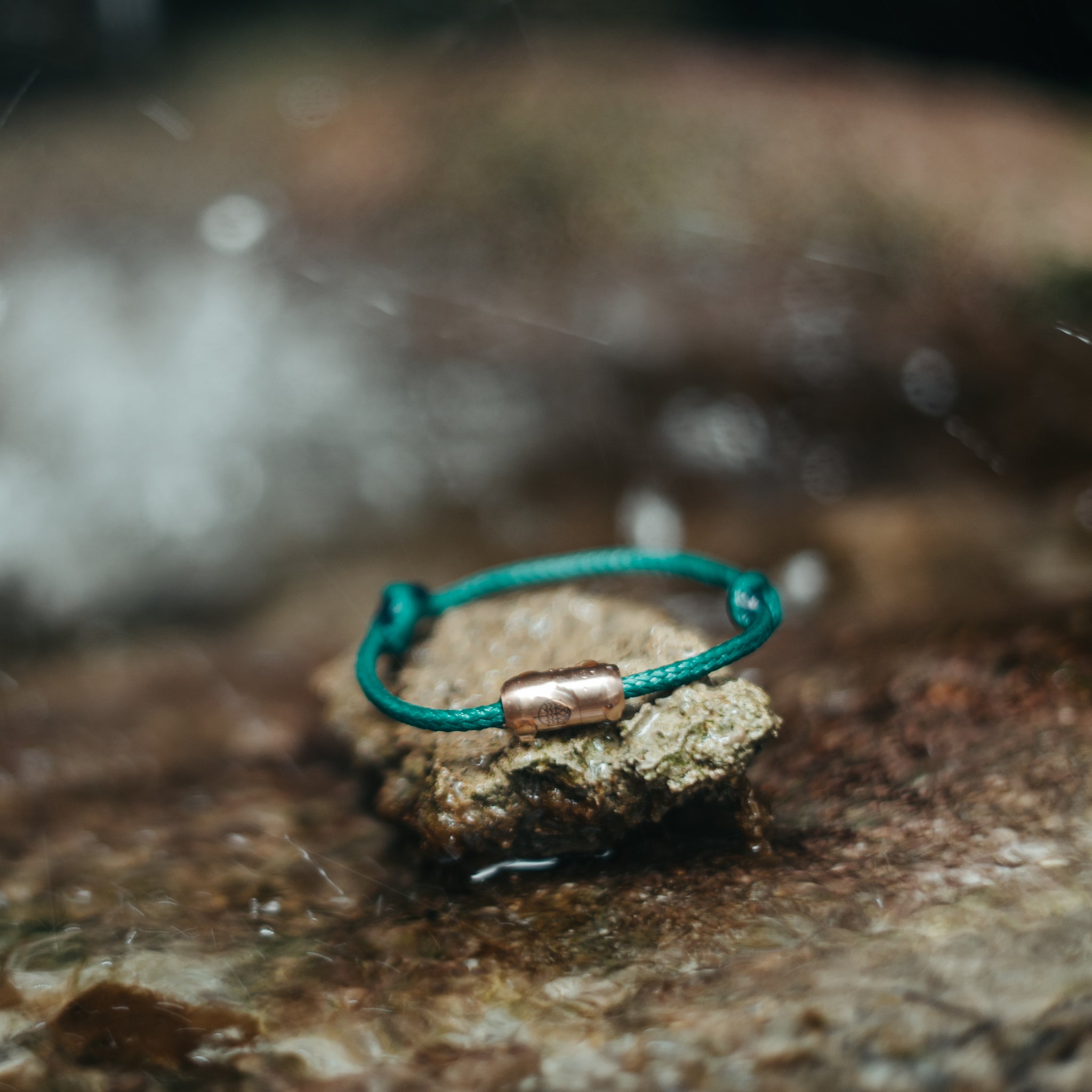 Ein grünes Armband mit einem Kupferverschluss liegt auf einem nassen Felsen im Freien.