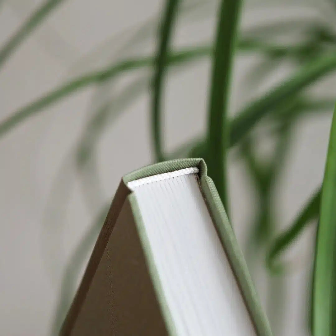 Ein geschlossenes Buch mit grünem Einband steht vor verschwommenem grünen Hintergrund aus Pflanzen.