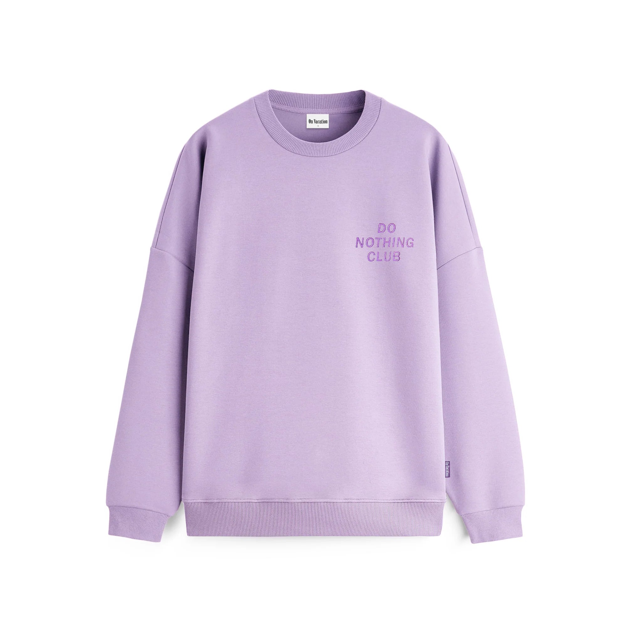Ein lavendelfarbenes Sweatshirt mit Rundhalsausschnitt, langen Ärmeln und der Aufschrift "DO NOTHING CLUB", die in kleinen Buchstaben auf der linken Brustseite eingestickt ist.