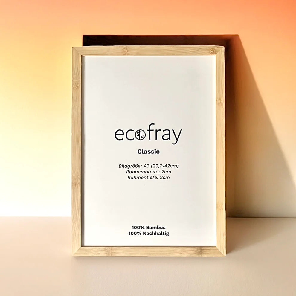 Ein hölzerner Bilderrahmen mit einem weißen Einsatz, der die Marke ecofray Classic und Produktdetails in deutscher Sprache zeigt, steht auf einer weißen Fläche vor einem Hintergrund mit Pfirsich- und Orangenverläufen.