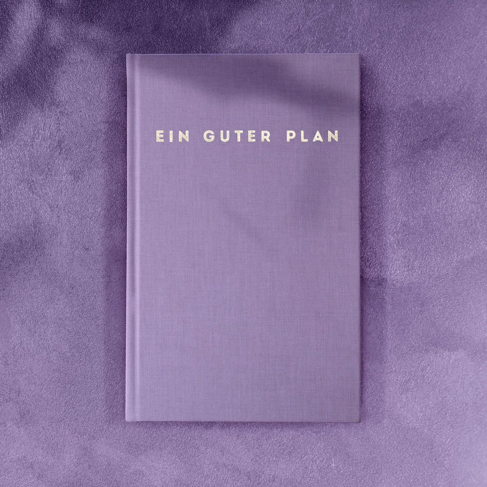Lila Buch mit der Aufschrift "EIN GUTER PLAN" auf lila Hintergrund.