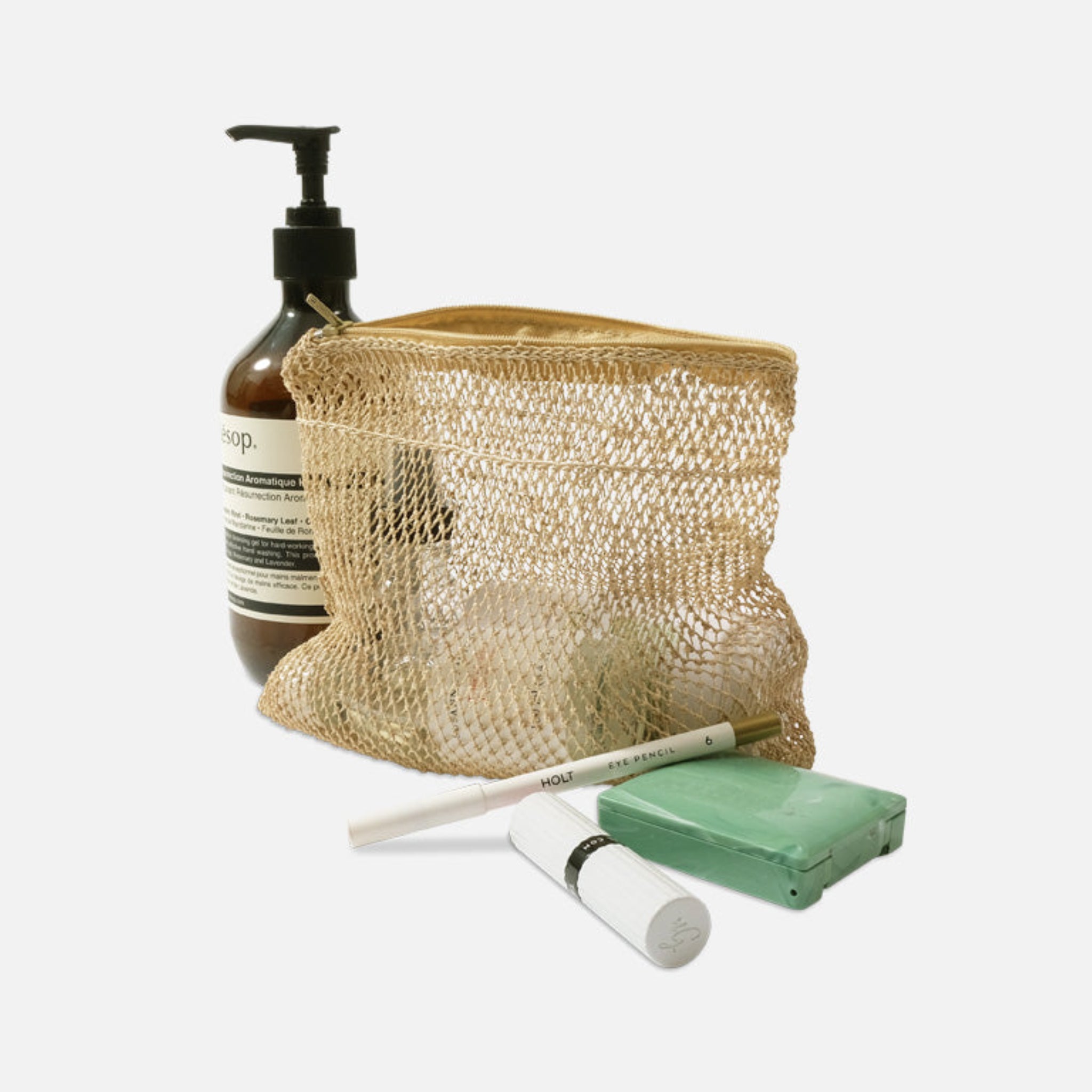 Kosmetikutensilien in einer Netztasche, einschließlich einer Pumpflasche, eines Lippenstifts, eines Stiftes und eines grünen Kästchens.