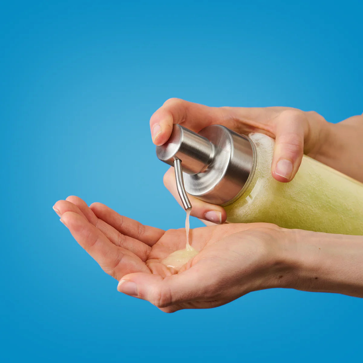 Eine Person, die gelbe Flüssigseife aus einer Pumpflasche in ihre offene Handfläche abgibt, mit blauem Hintergrund.