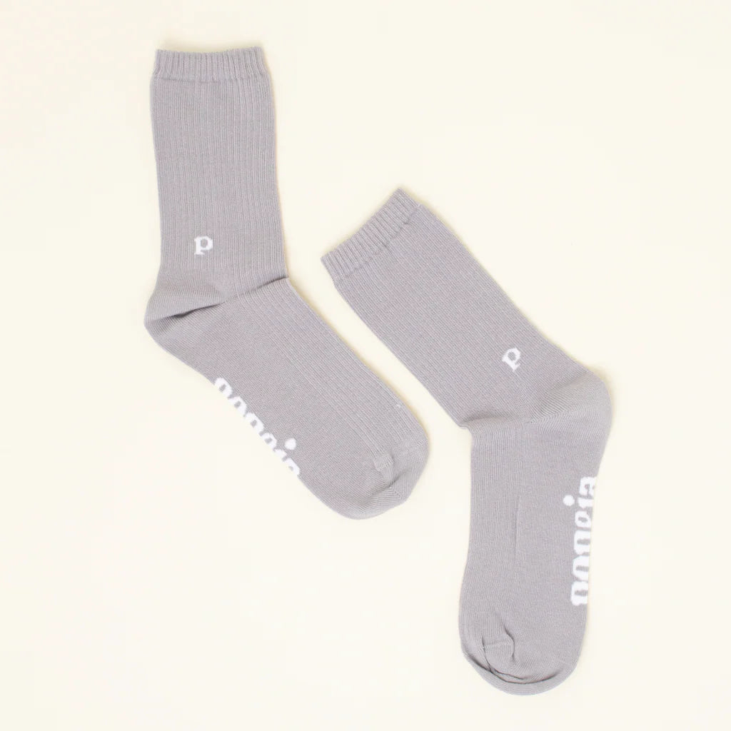 Ein Paar hellgraue Socken mit gerippten Bündchen, auf denen in der Nähe des Knöchels ein kleines weißes "p" und an der Seite des Fußes das Wort "Paranoia" zu lesen ist.