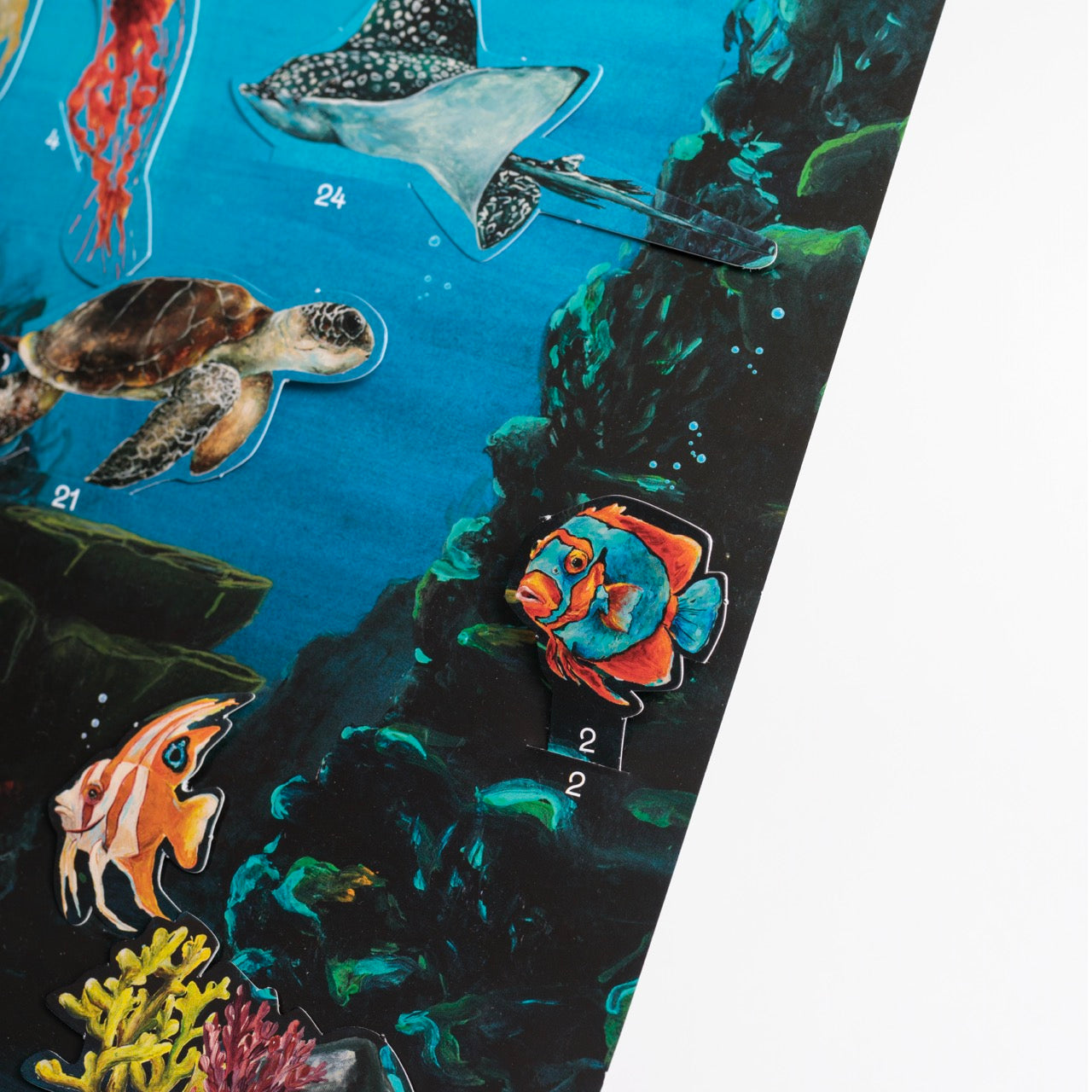 Eine Nahaufnahme einer illustrierten Meeresszene mit verschiedenen Meeresbewohnern, darunter eine Schildkröte, ein Rochen, ein Kaiserfisch und ein bunter Fisch mit der Nummer 2 vor einem dunkelblauen Hintergrund mit Korallen und Felsen.