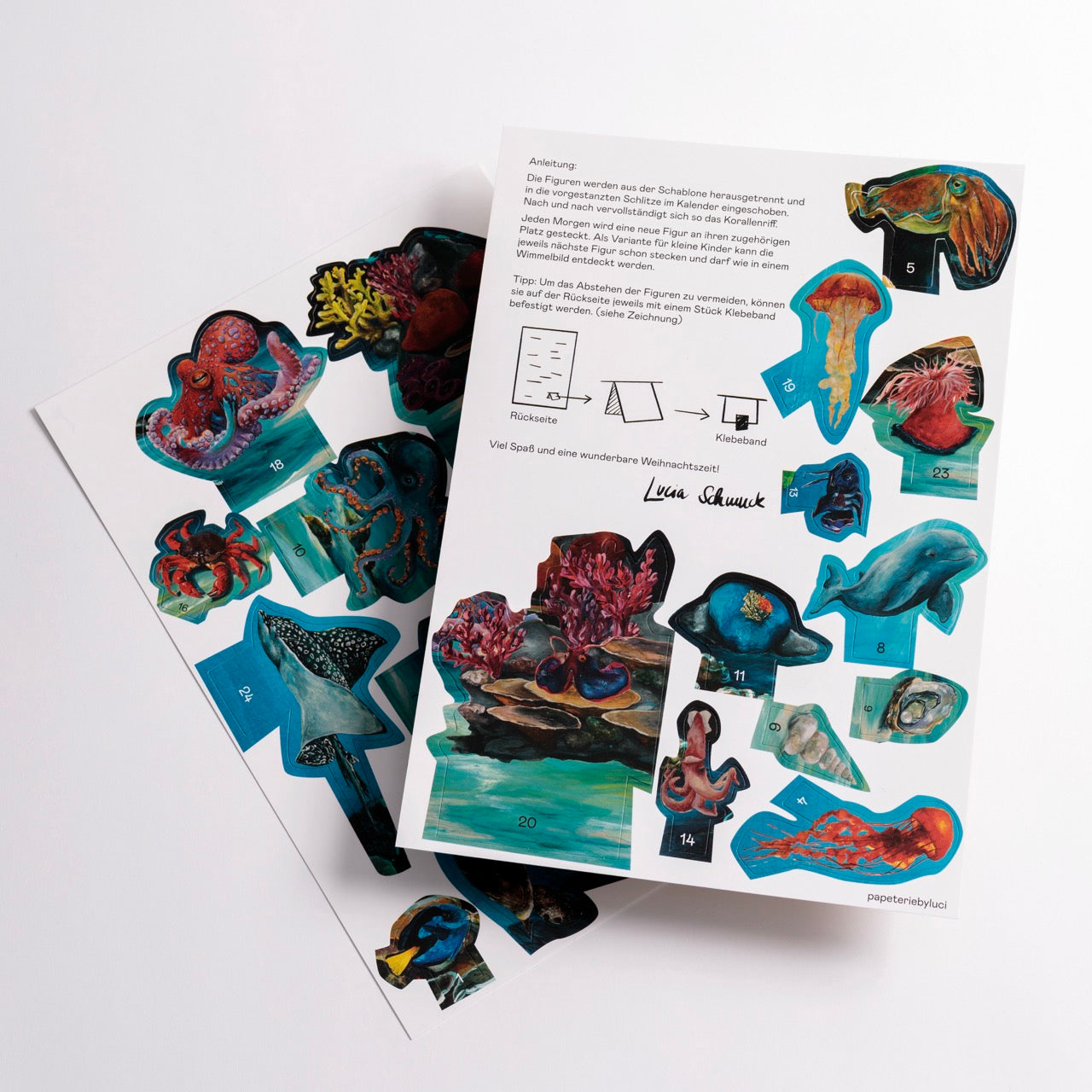 Zwei Blätter mit farbenfrohen, ausgeschnittenen Illustrationen von verschiedenen Meeresbewohnern wie Fischen, Quallen, Kraken, Haien und Korallen, die sauber auf einem weißen Hintergrund angeordnet sind, wobei einige deutsche Texte und Diagramme sichtbar sind.