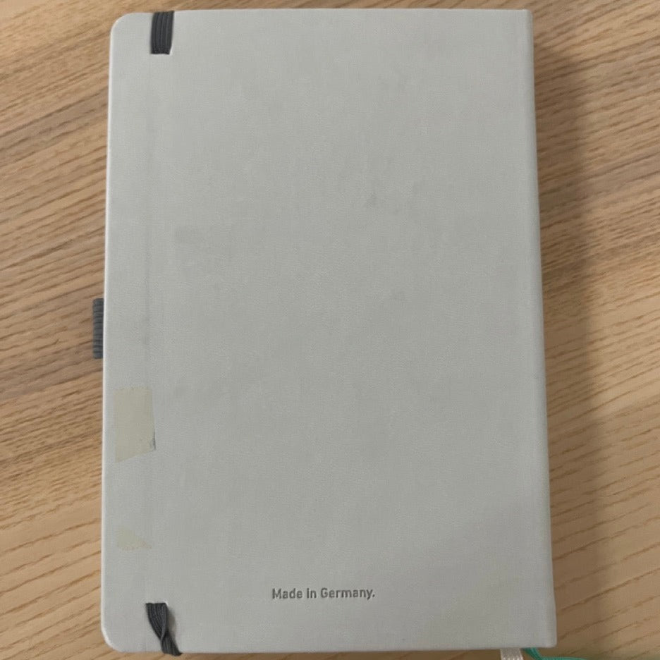 Graues Notizbuch mit elastischem Band auf einem Holztisch, mit der Aufschrift "Made in Germany".