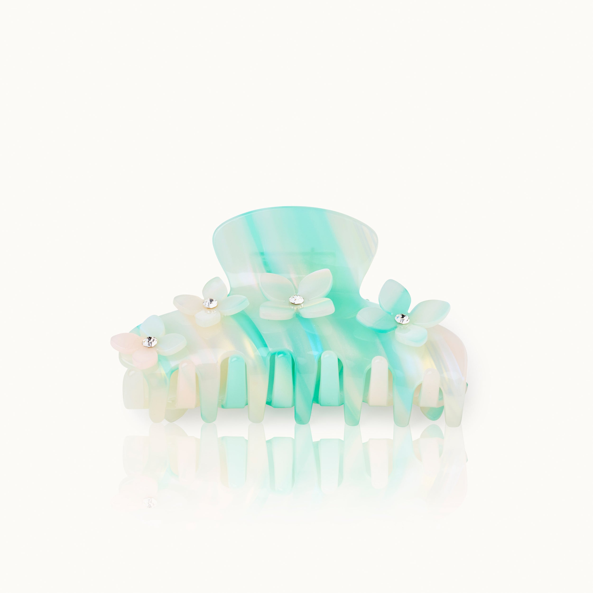Eine pastellblau und grün marmorierte Haarklammer mit kleinen, zarten Blumenverzierungen, jede mit einem glänzenden Edelstein in der Mitte, auf einem weißen Hintergrund.