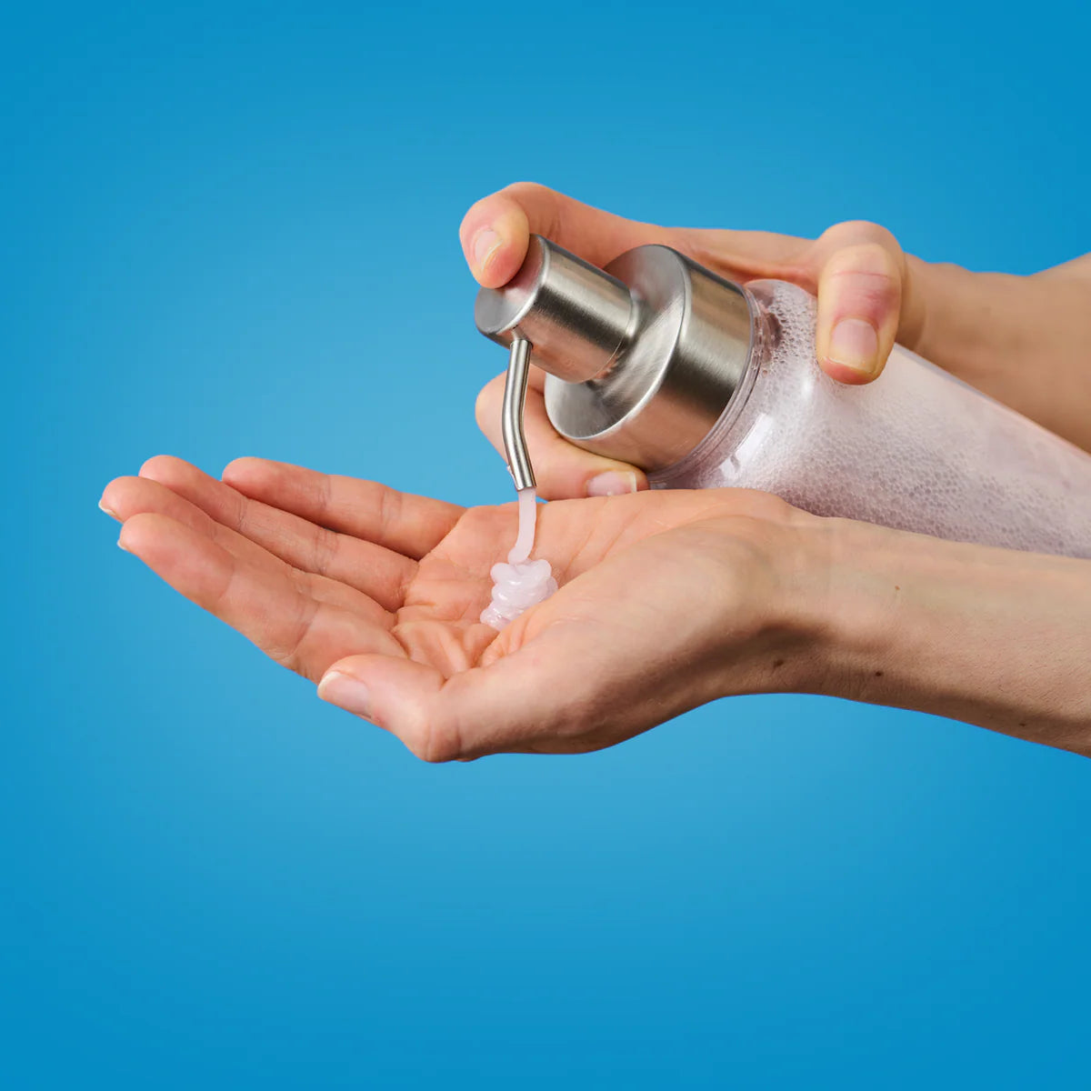 Eine Person spendet klare Flüssigseife oder Desinfektionsmittel aus einer Pumpflasche auf ihre offene Handfläche vor einem schlichten blauen Hintergrund.