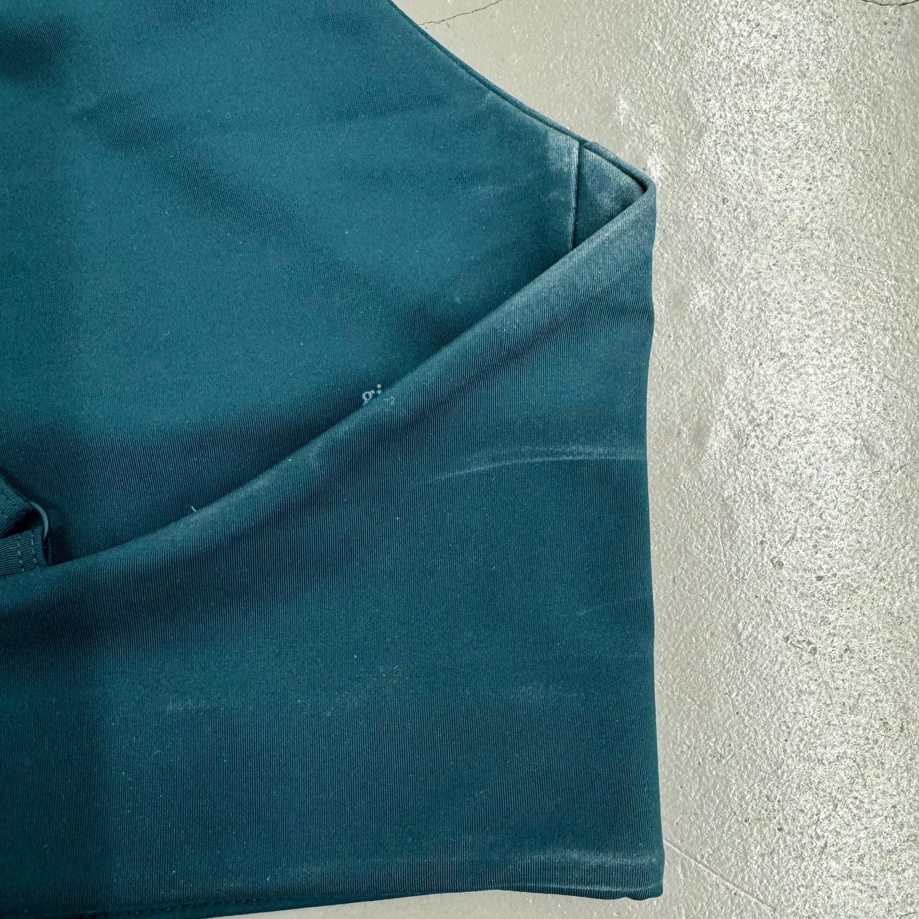 Eine dunkelgrüne Stoffhose liegt auf einem hellen, strukturierten Boden.