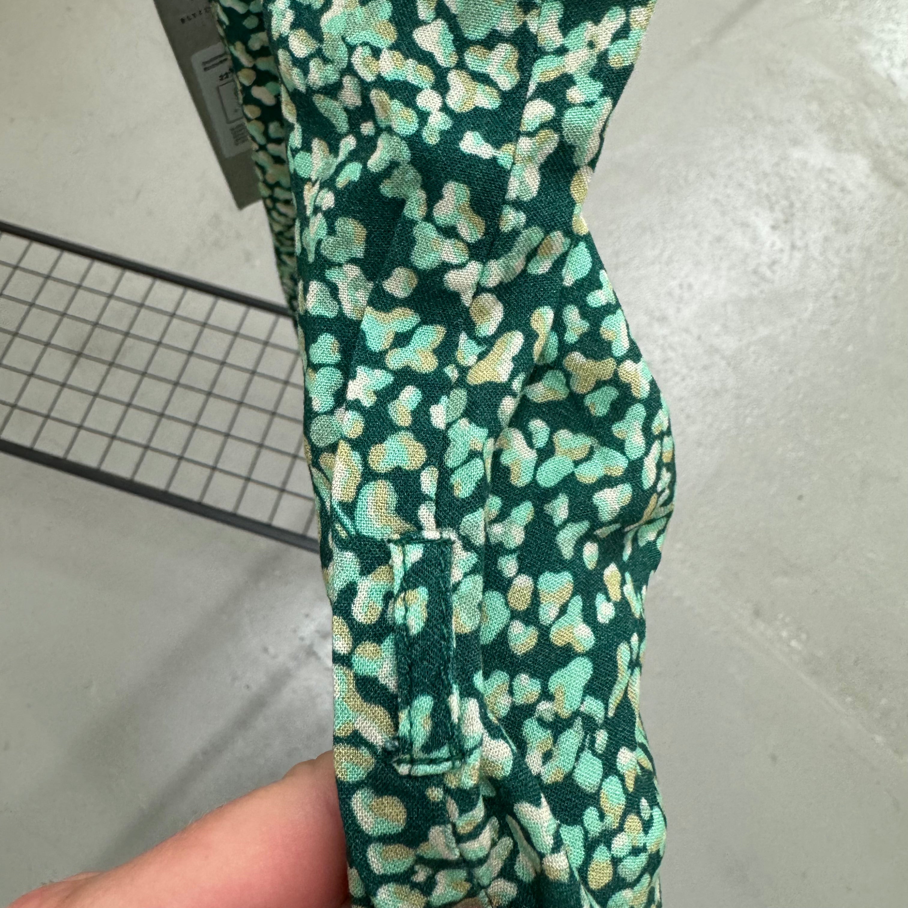 Grünes Stoffmuster mit hellen Tupfen in Nahaufnahme, gehalten von einer Hand.