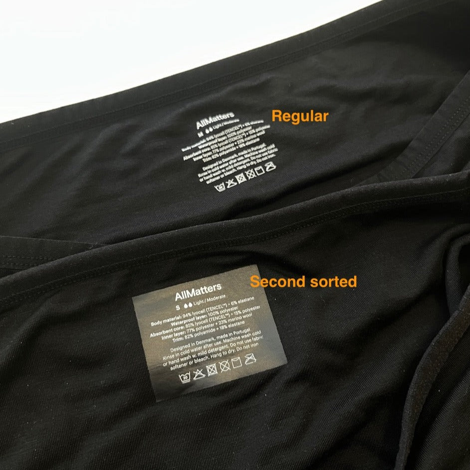 Zwei schwarze Kleidungsstücke mit Innenetiketten von "AllMatters", die als "Regular" und "Second sorted" bezeichnet sind.