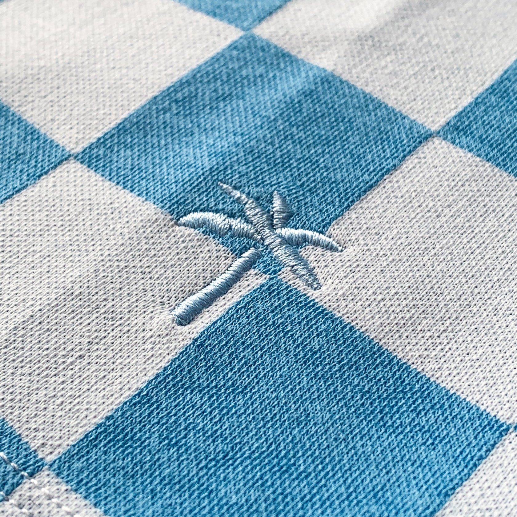 Nahaufnahme eines blau-weiß karierten Stoffes mit einem kleinen, weiß gestickten Palmenmuster auf einem der weißen Quadrate.