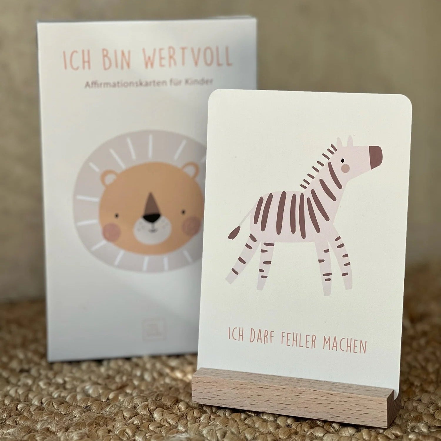 Gezeigt wird ein Satz deutscher Bejahungskarten für Kinder. Die vordere Karte zeigt ein illustriertes Zebra und den Text "ICH DARF FEHLER MACHEN." Das Feld dahinter zeigt einen Löwen und den Text "ICH BIN WERTVOLL.".