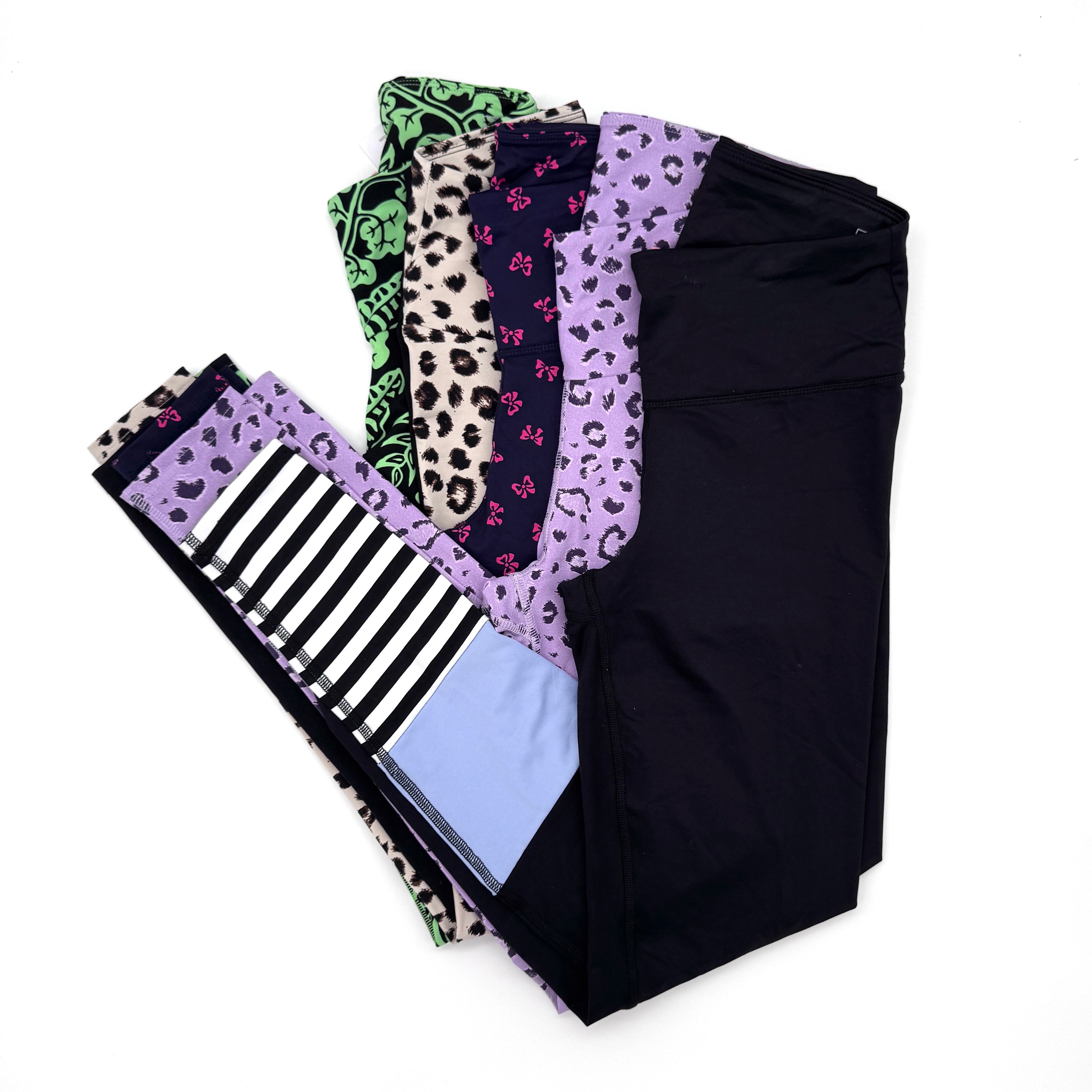 Vier Paar fächerförmig angeordnete Leggings mit unterschiedlichen Mustern wie Tiermotiven, Streifen und Farbblöcken in Schwarz-, Lila-, Grün-, Creme- und Blautönen auf einem weißen Hintergrund.