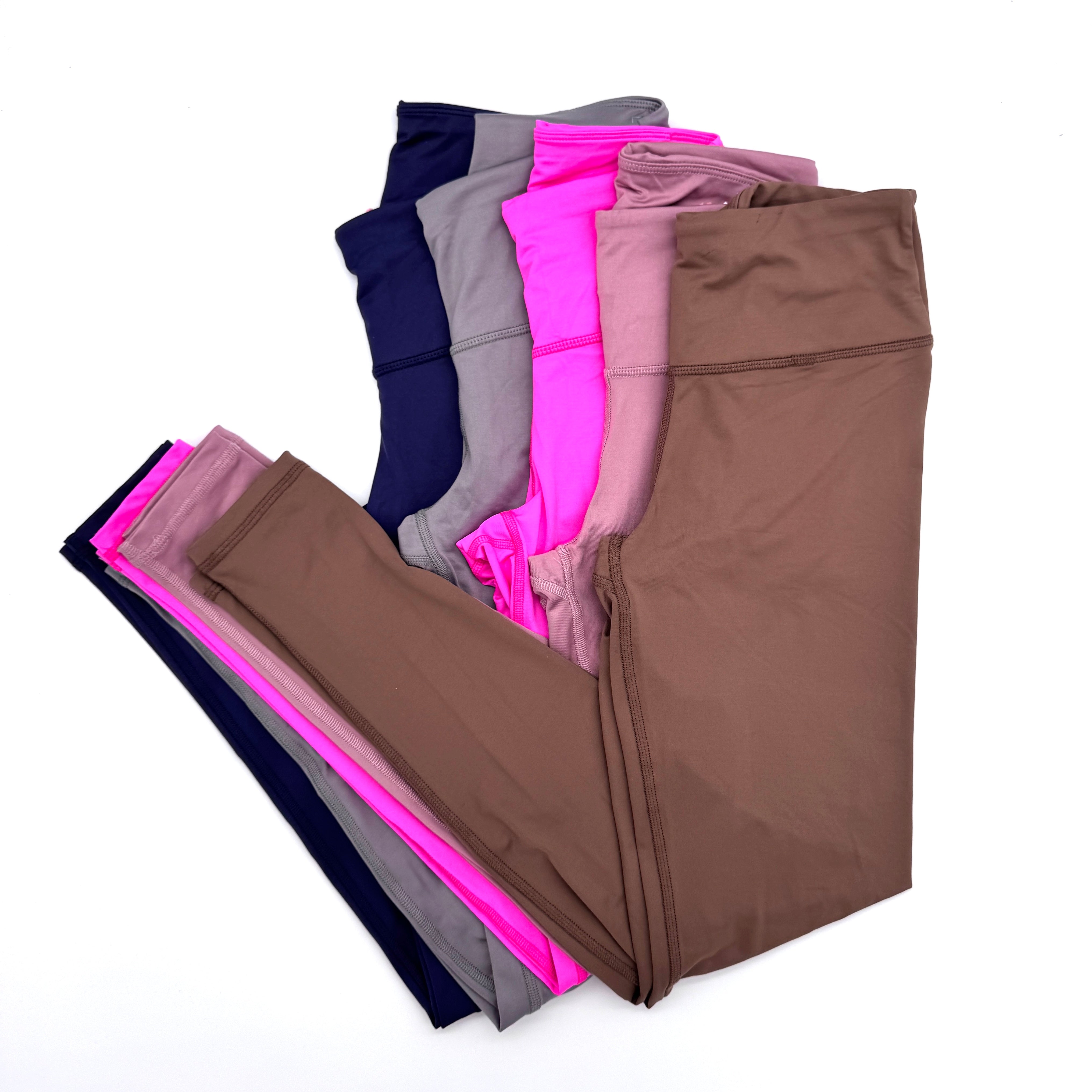 Ein ordentlich gestapelter Stapel von fünf Paar Leggings in verschiedenen Farben, darunter braun, rosa, grau, marineblau und lila, auf einem weißen Hintergrund.