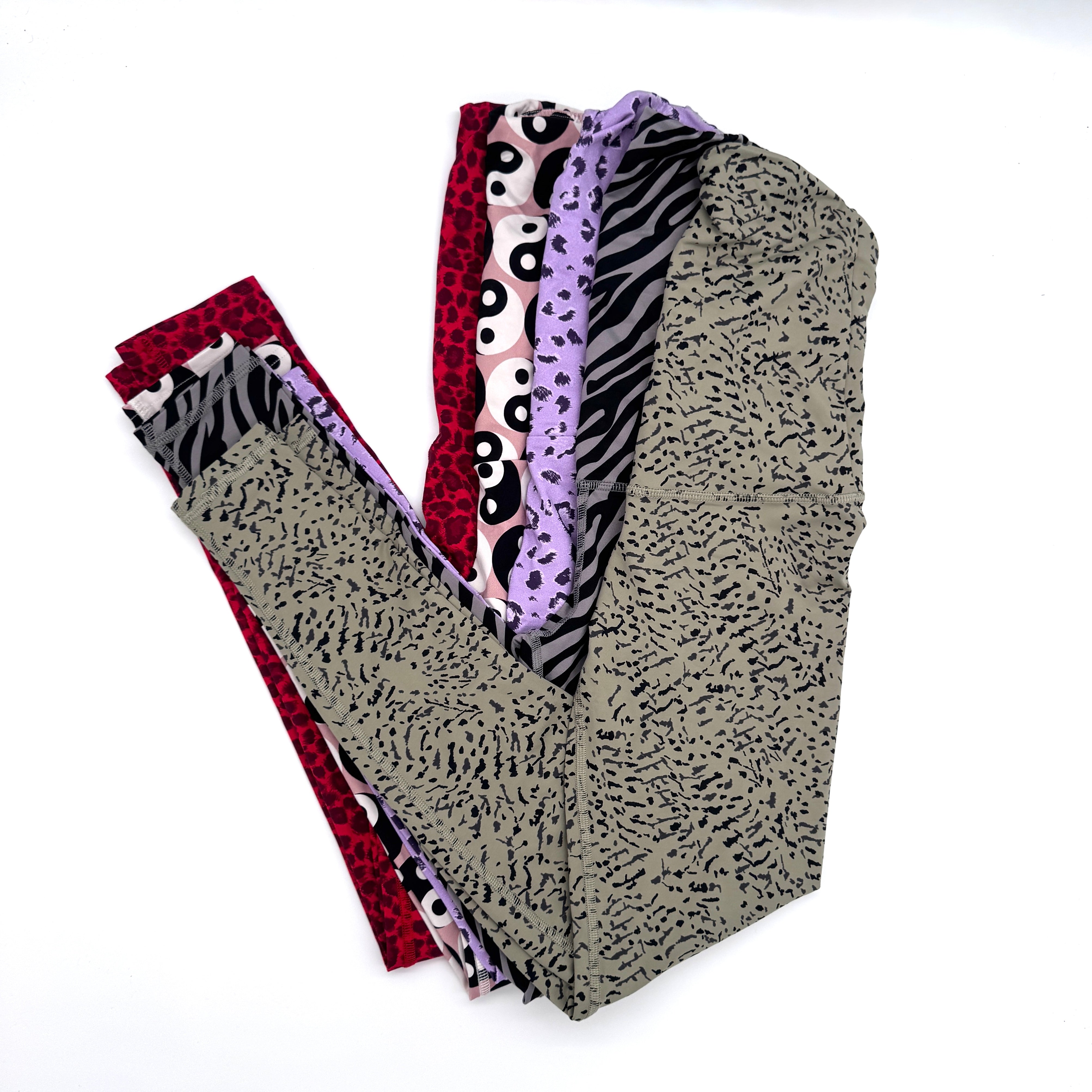 Vier Paar gefaltete Leggings mit unterschiedlichen Mustern, darunter roter Leopardenprint, schwarz-weißer Tierprint, lila mit schwarzen Punkten und hellgrün mit kleinen schwarzen Punkten, sind auf weißem Hintergrund übereinander angeordnet.