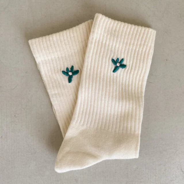 Ein Paar gerippte, wollweiße Socken mit einem kleinen gestickten grün-weißen Blumenmuster am oberen Rand.