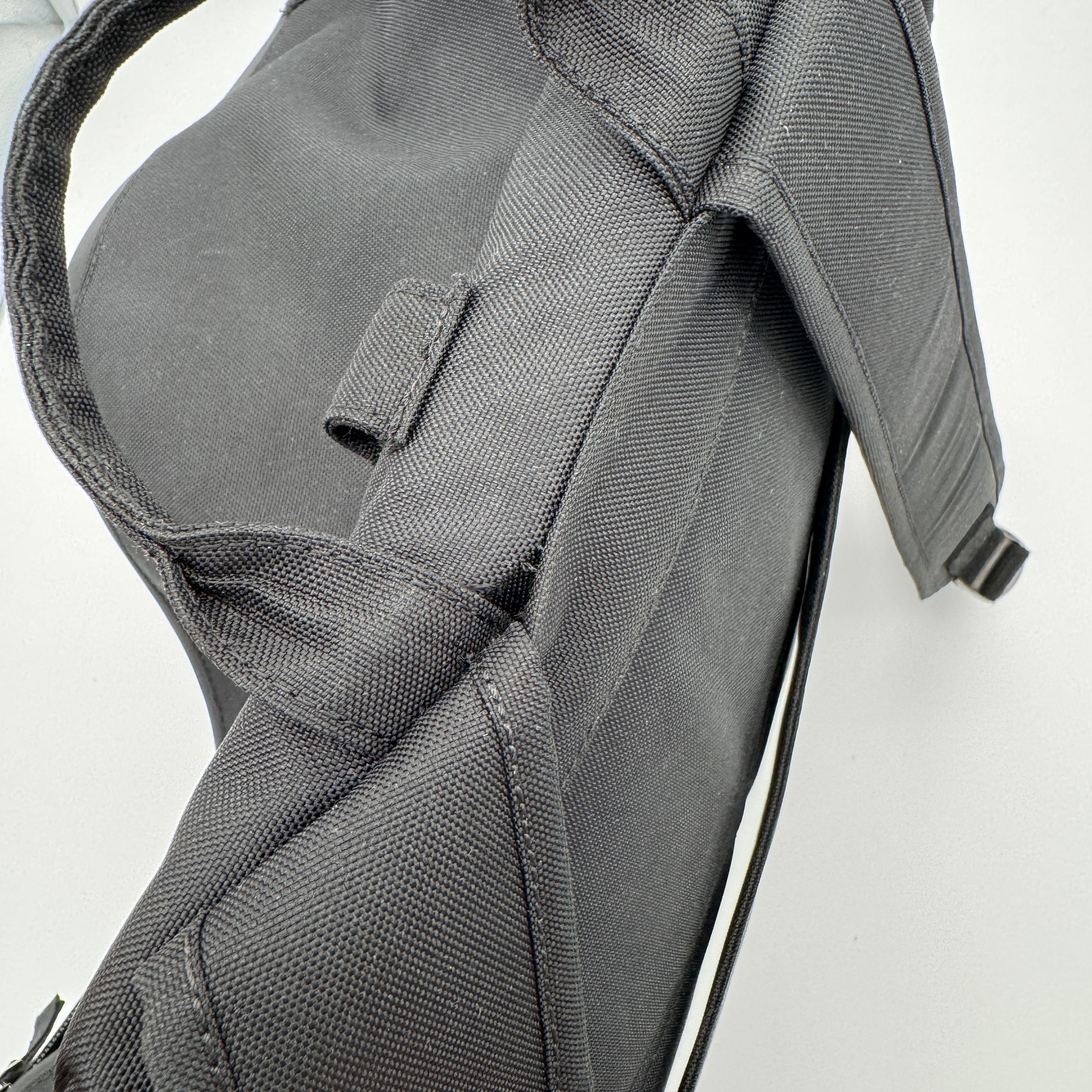 Nahaufnahme eines schwarzen Rucksacks, die den Griff, den gepolsterten Schultergurt und den strukturierten Stoff auf einer hellen Fläche zeigt.