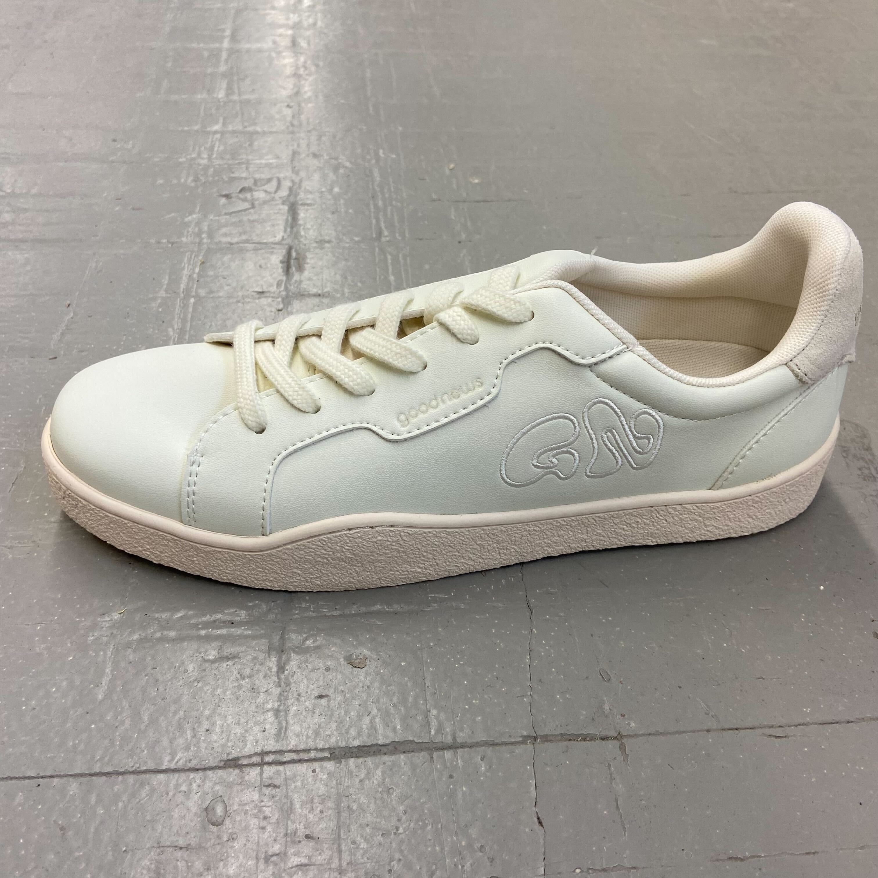 Ein weißer Turnschuh auf einem grauen Boden, mit seitlichem Logo und Schnürsenkeln.
