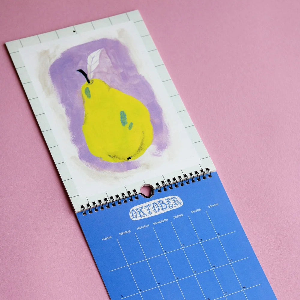 Ein Wandkalender, der bis Oktober geöffnet ist und das Bild einer gelben Birne mit weißem Blatt auf violettem Hintergrund zeigt, das auf einer rosafarbenen Oberfläche abgebildet ist.