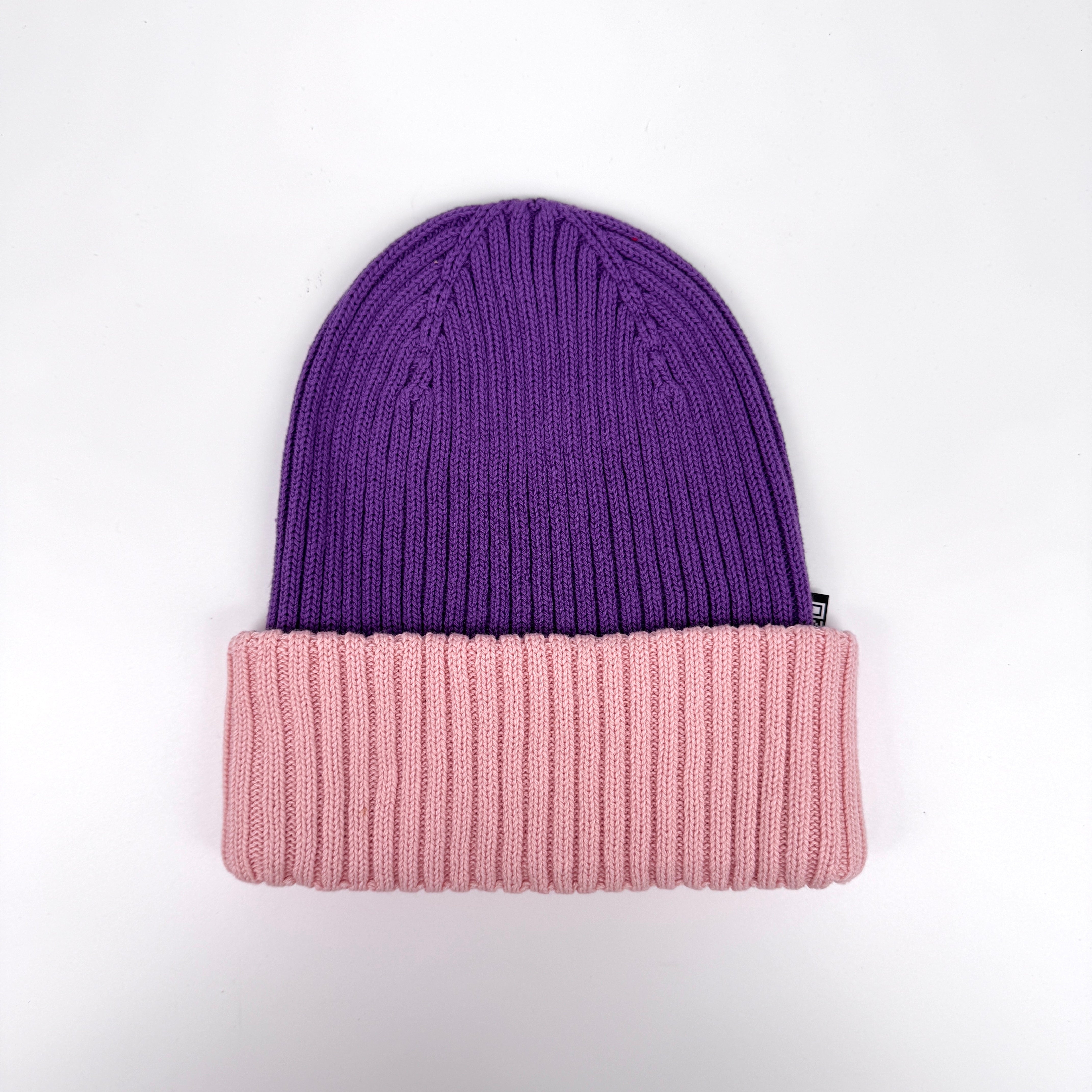 Rippenstrickmütze mit violettem Oberteil und breiter, gefalteter rosa Krempe auf einfarbig weißem Hintergrund.