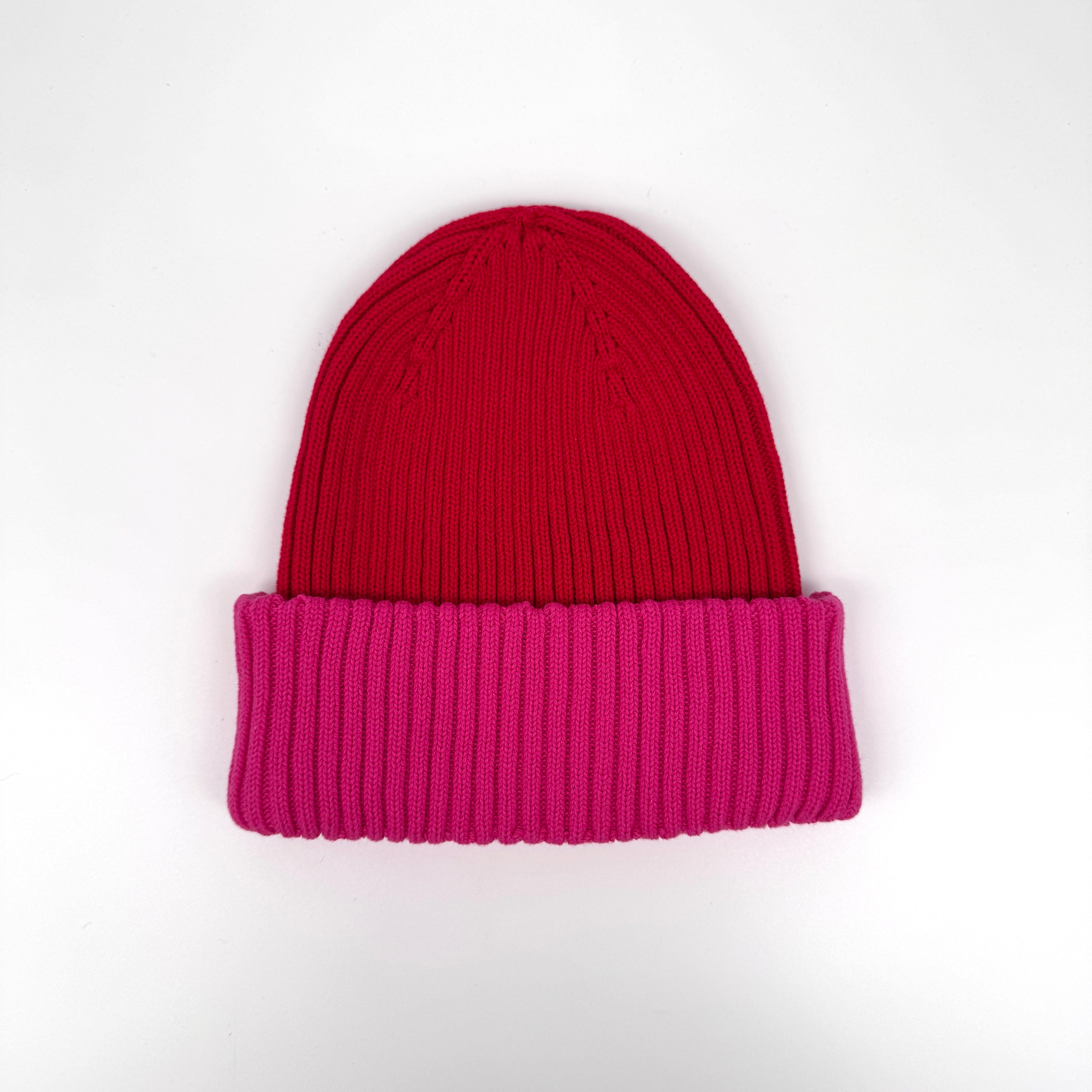 Eine Strickmütze mit tiefrotem Scheitel und breiter, leuchtend rosa gefalteter Krempe auf einfarbig weißem Hintergrund.