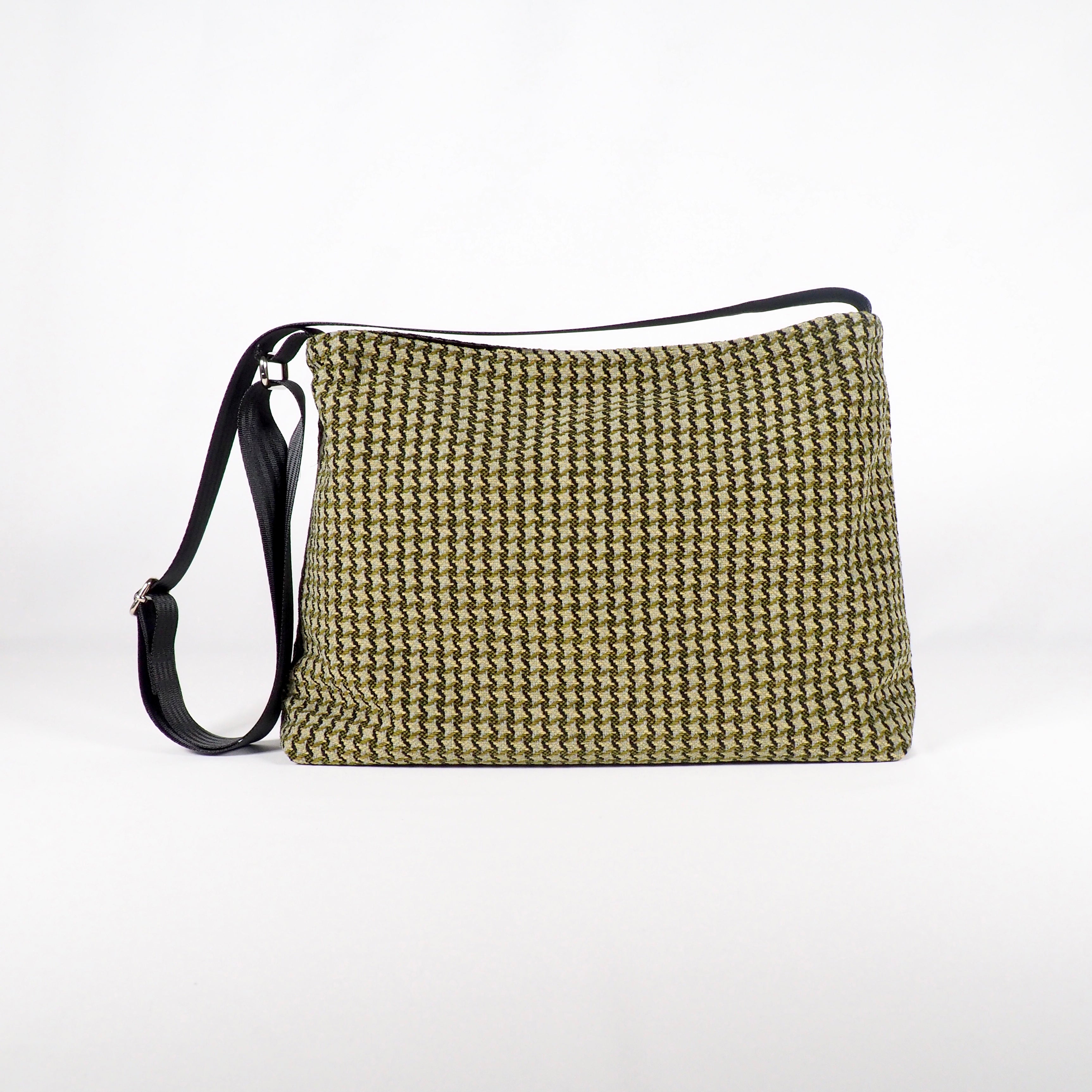 Beige Schultertasche mit schwarzem, gewobenem Muster und verstellbarem Riemen vor einem weißen Hintergrund.