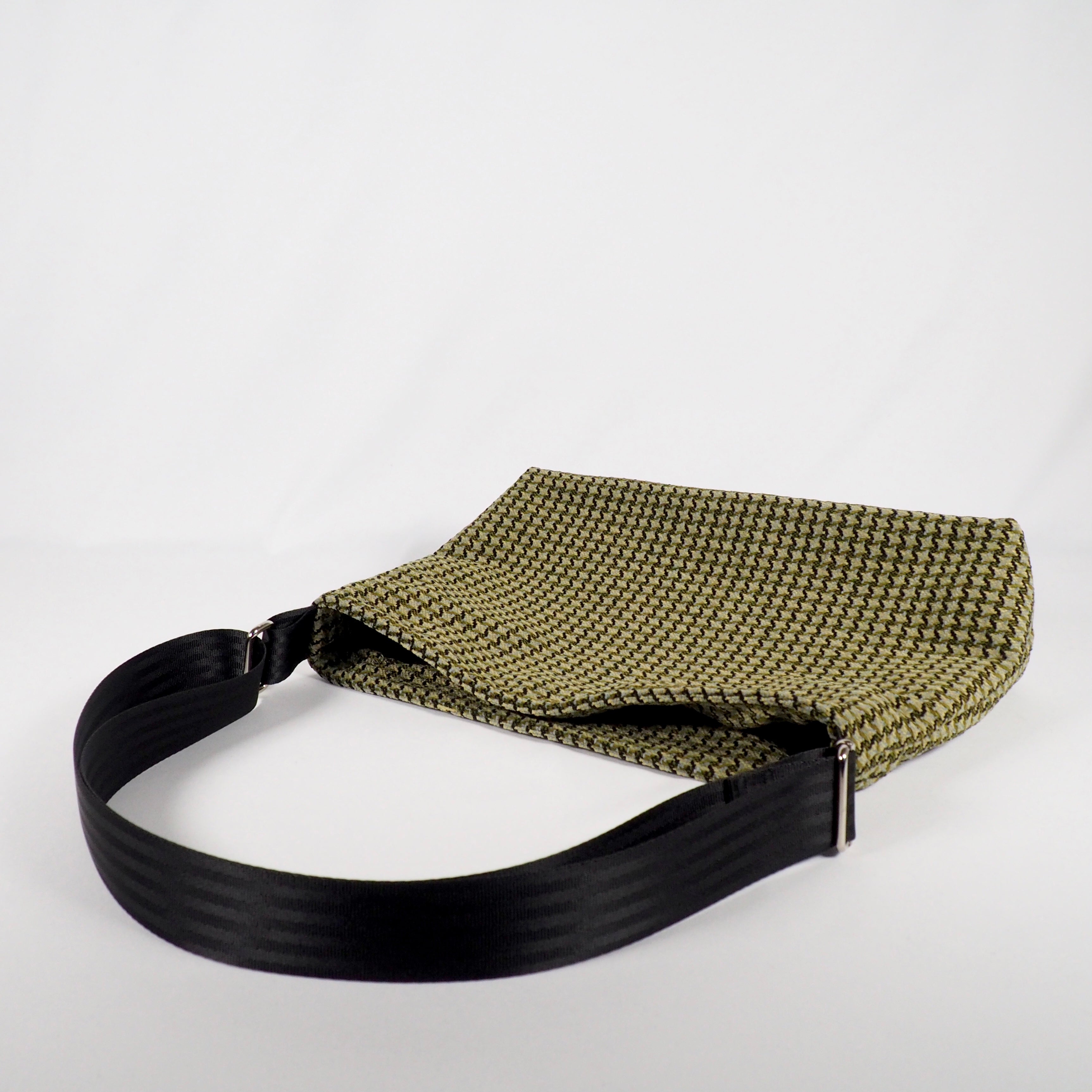 Olivegrüne Tasche mit schwarzem Riemen auf weißem Hintergrund.