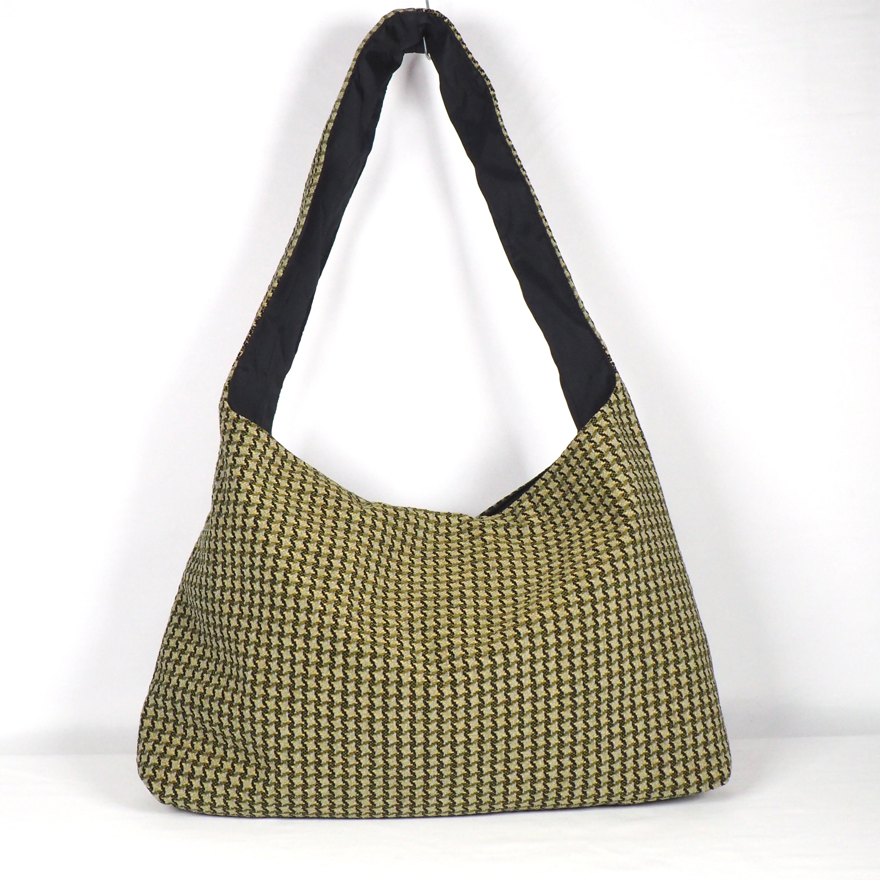 Eine große, weiche Umhängetasche im Hobo-Stil mit schwarz-goldenem Hahnentrittmuster und breitem Riemen. Das Innenfutter ist schwarz. Die Tasche ist vor einem schlichten weißen Hintergrund abgebildet.